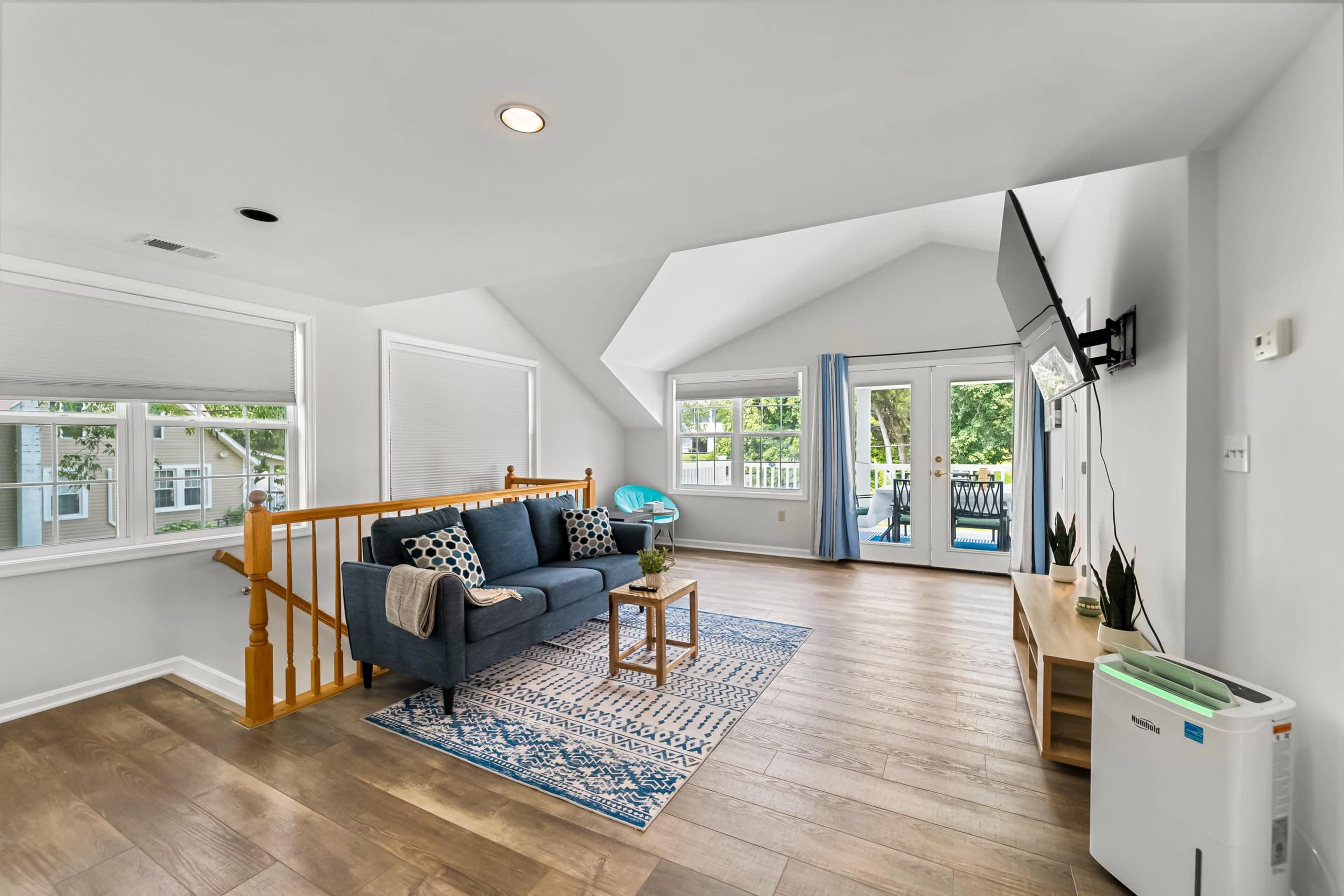 A cozy living space with a gray sofa, a patterned rug, and large windows leading to a deck.
