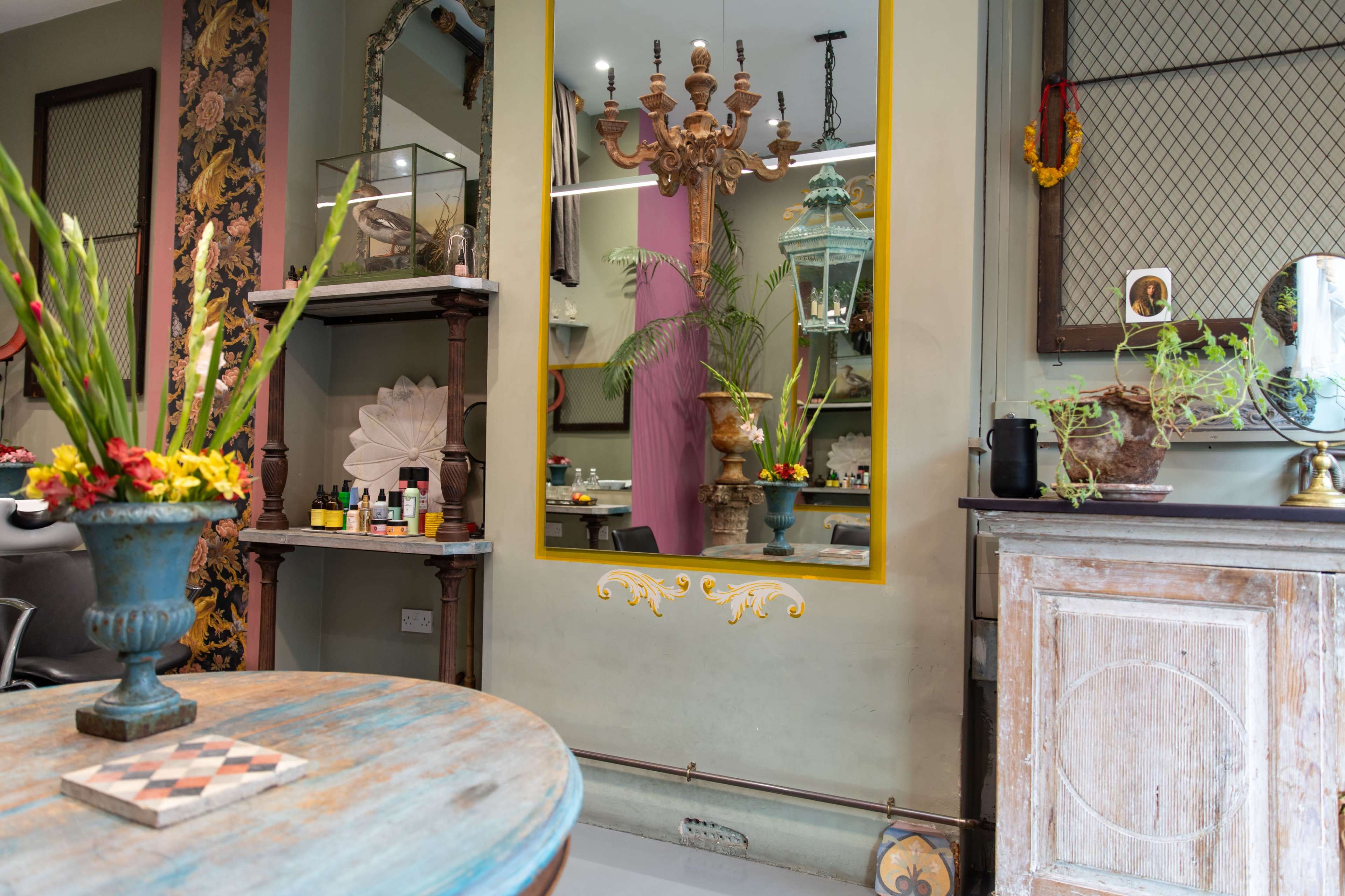 The image features a salon interior with decorative elements, including a large mirror, potted plants, a chandelier, and a rustic table.