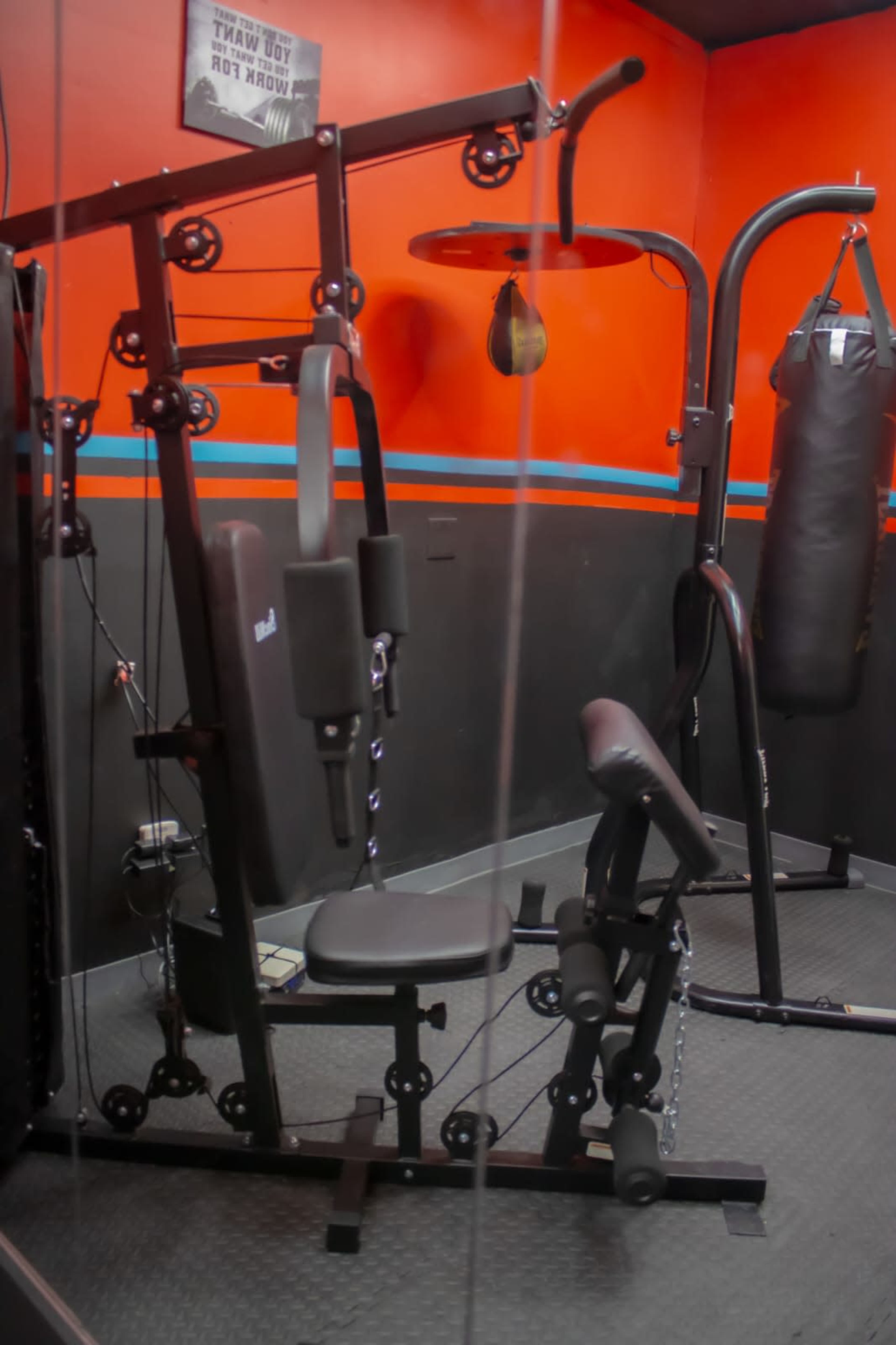 A gym room featuring a multi-station weight machine, a punching bag, and an upright exercise bike against a red and black wall.