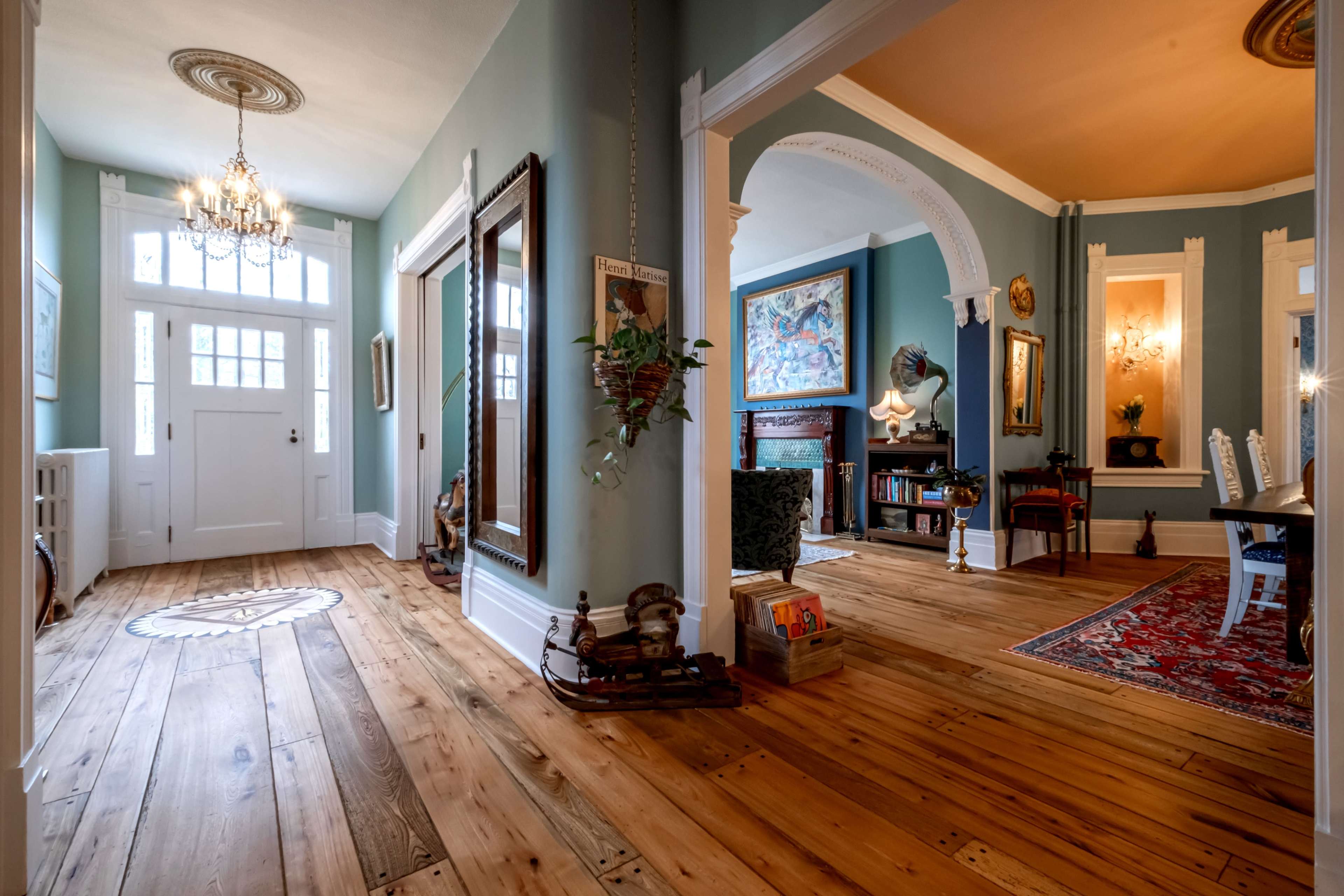 A spacious entryway with wooden flooring, a chandelier, and an arched passage leading to a brightly lit living area.