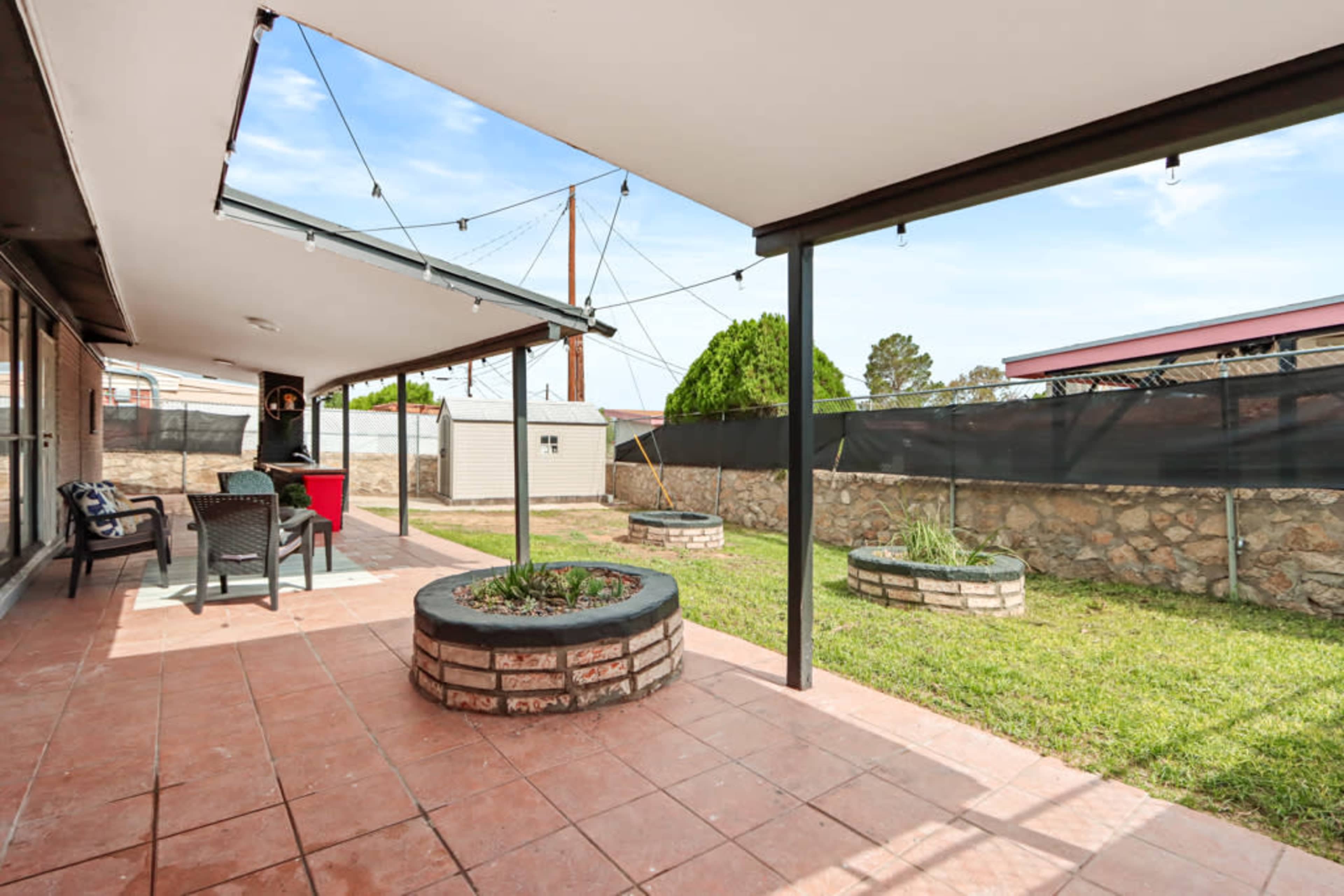 A covered outdoor patio area with stone planters and a grassy space, bordered by a wall.