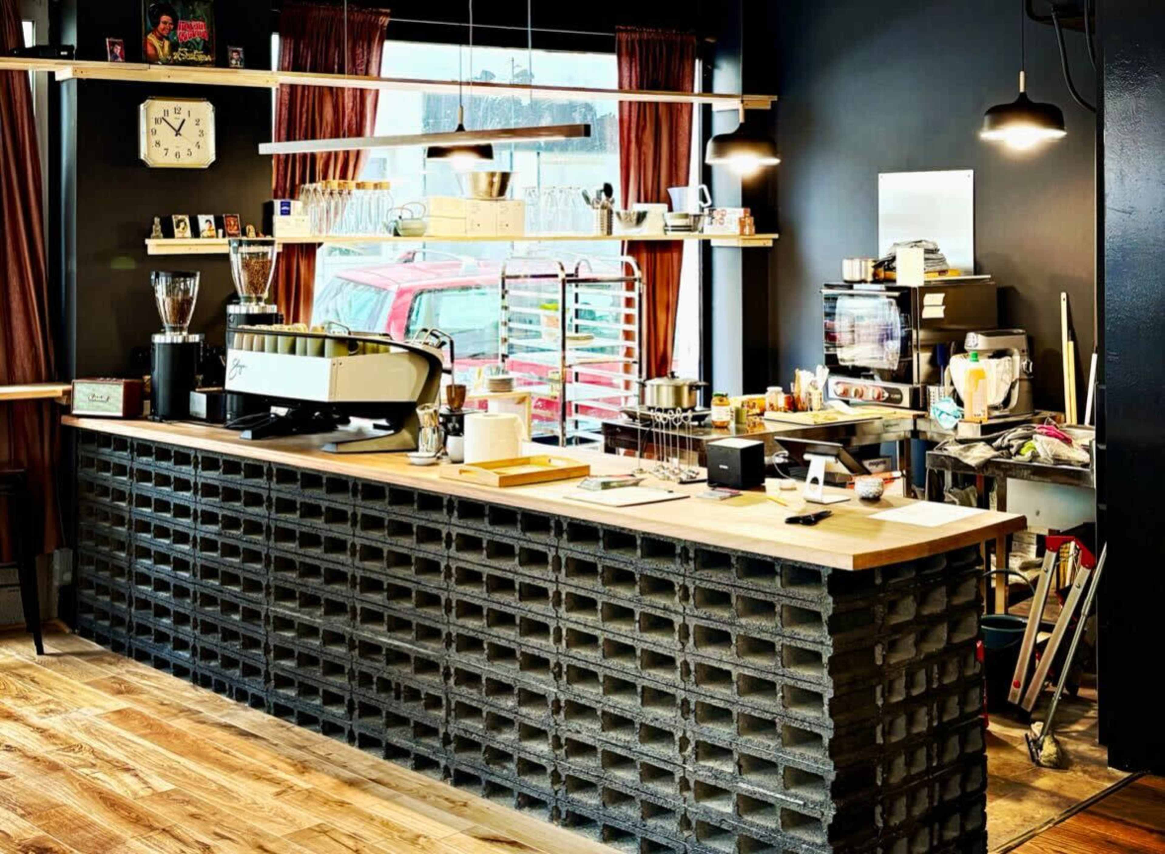 A coffee shop features a wooden counter built on a base of concrete blocks, with shelves displaying various coffee-making equipment and supplies.