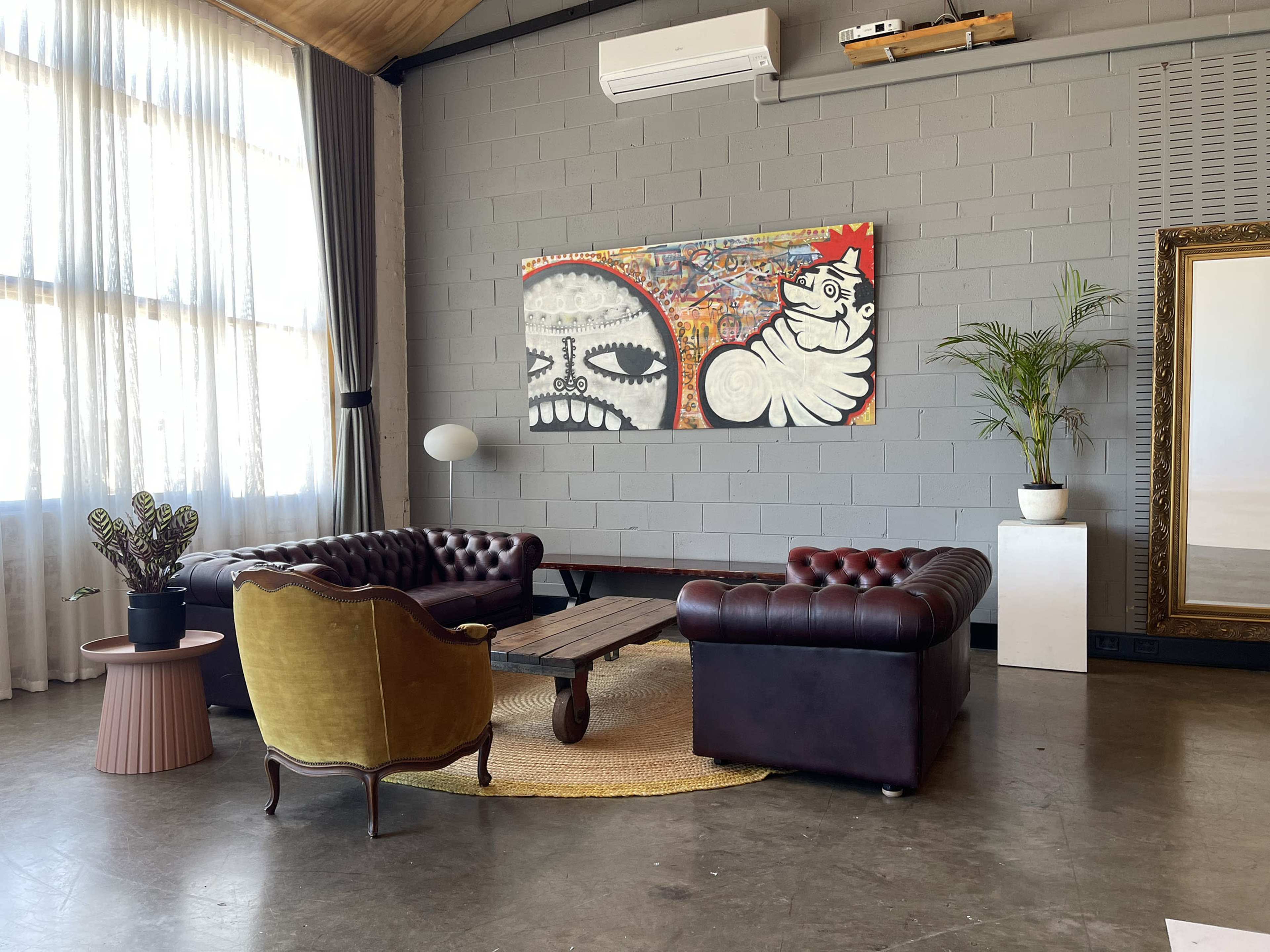The image depicts a stylish interior space featuring two leather sofas, a wooden coffee table, a potted plant, and an abstract painting on the wall.