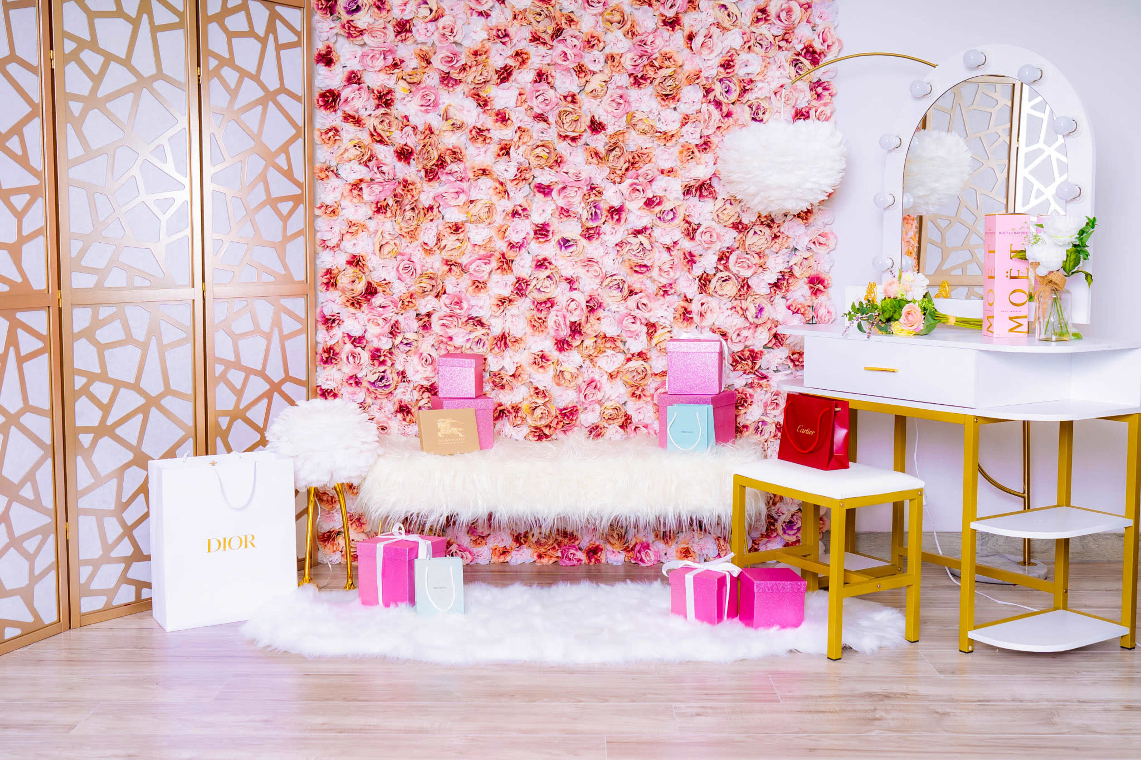 The scene features a bright and stylish vanity area with a floral backdrop, a white fur rug, and various gift boxes arranged on a white bench.