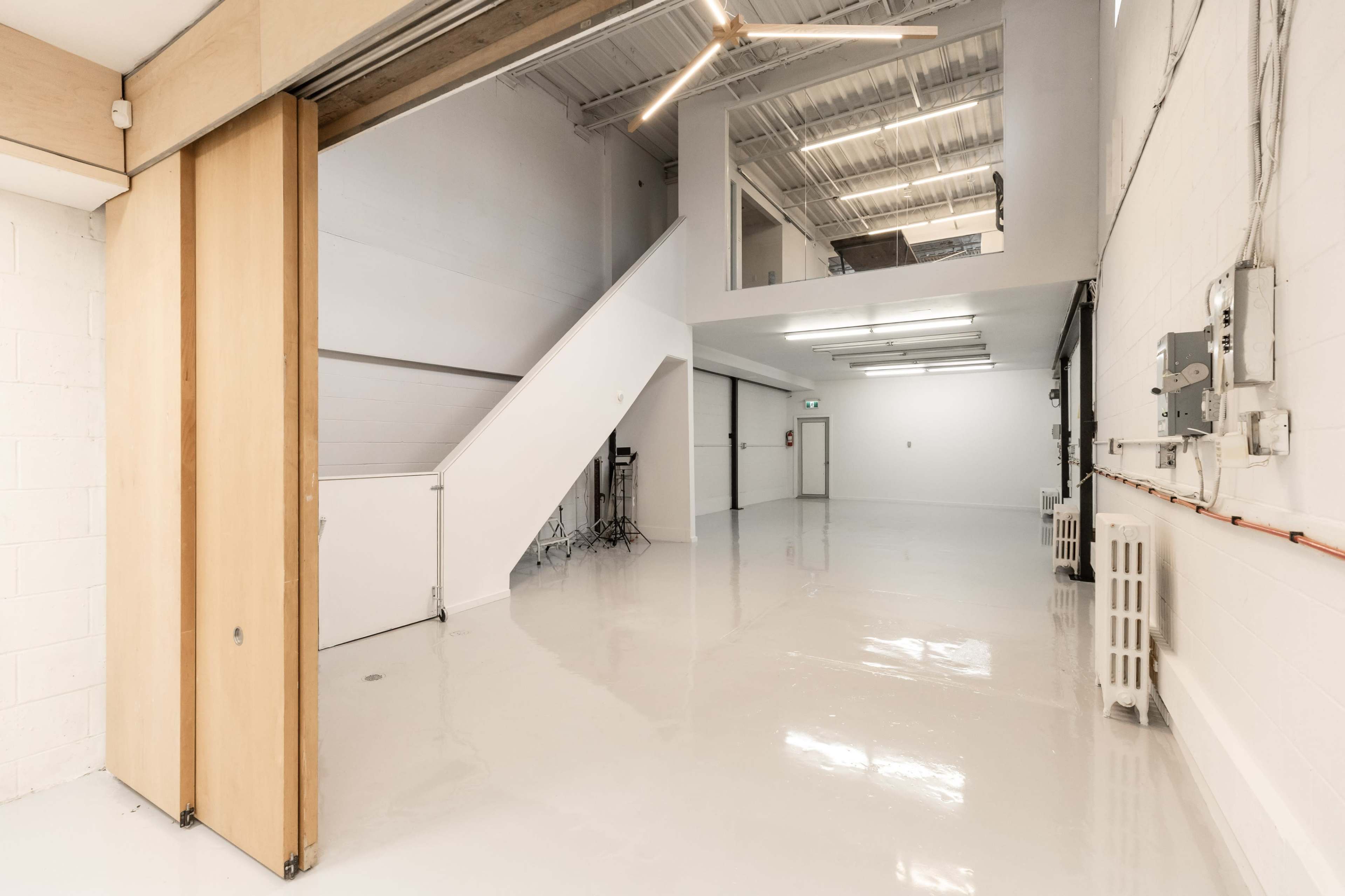 The image shows an empty, modern interior space with polished white floors, a staircase, and large overhead lights.