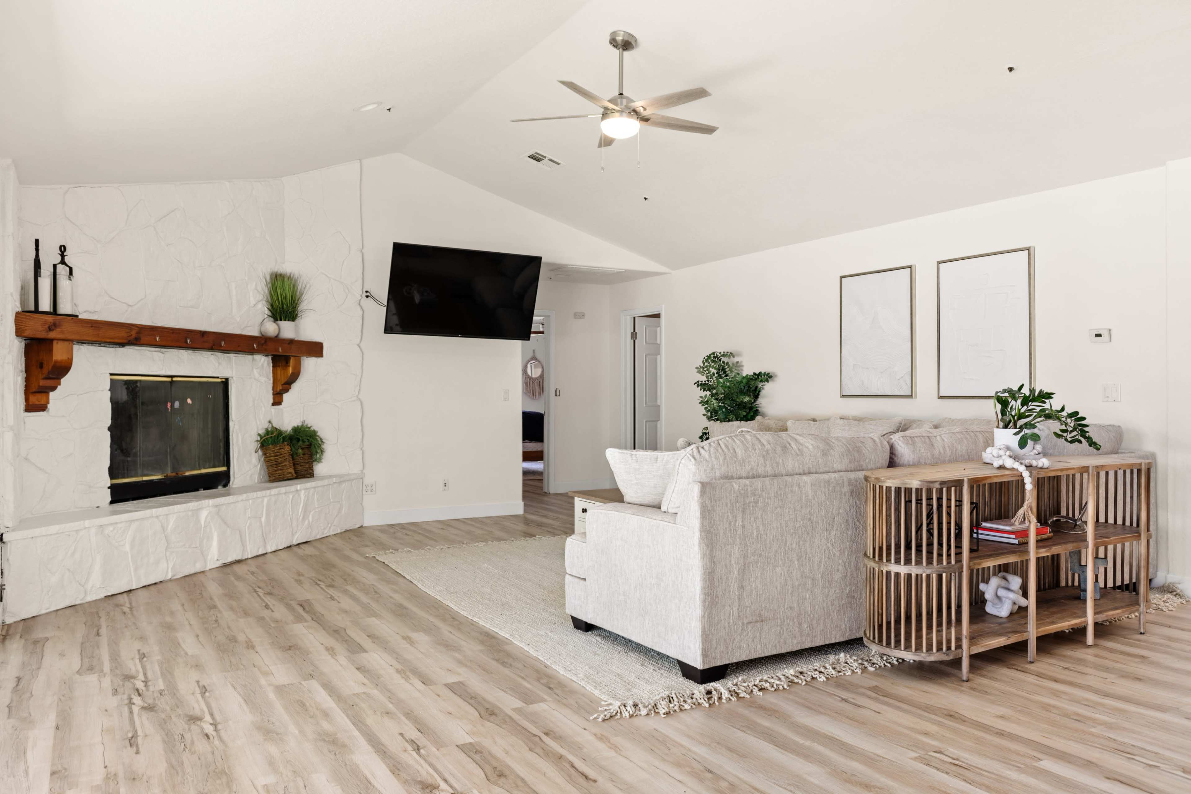 The image depicts a modern living room featuring a light-colored sofa, a wooden coffee table, and a fireplace with a TV mounted above it.