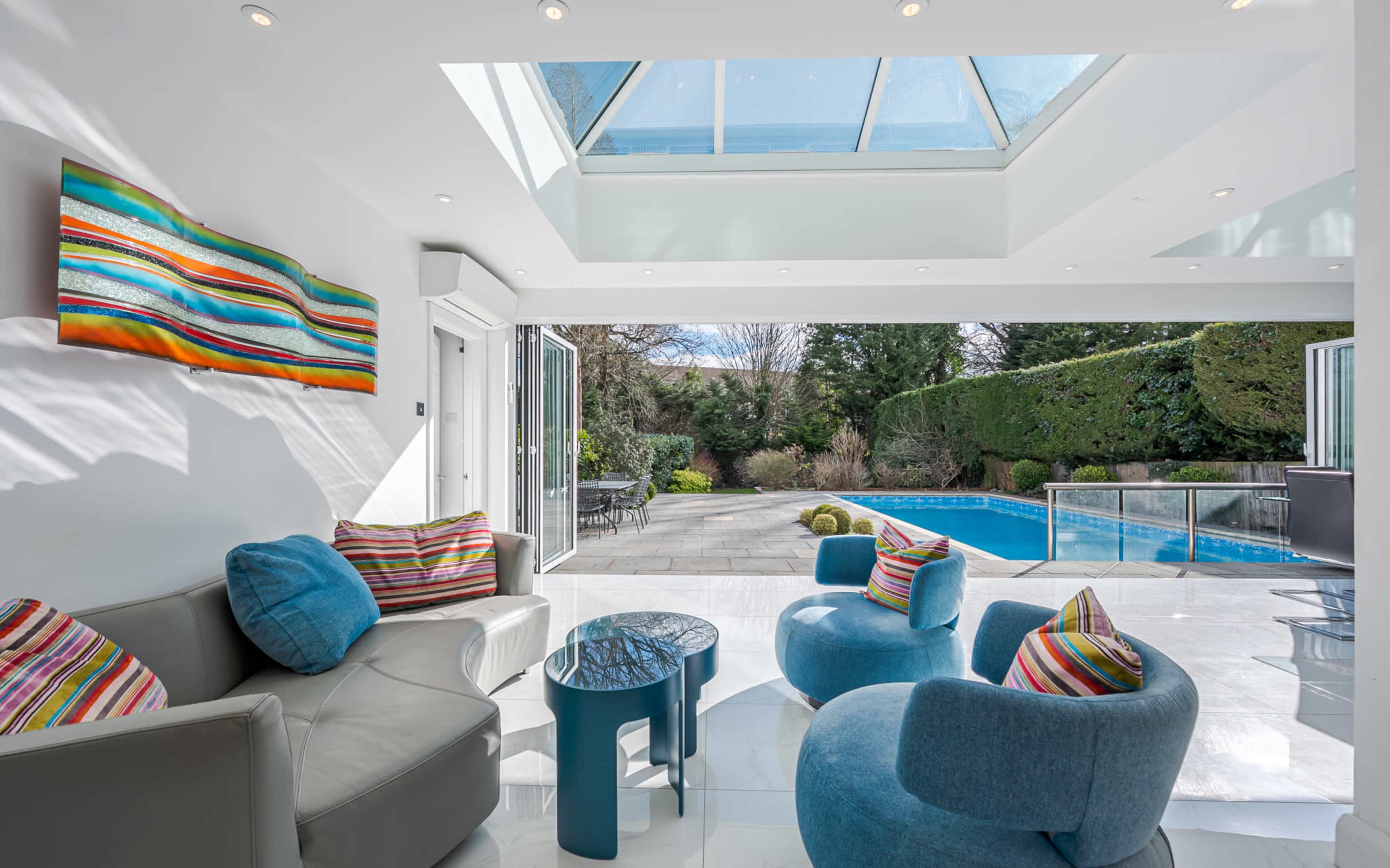A modern living room features colorful cushions and a view of a pool through large glass doors.