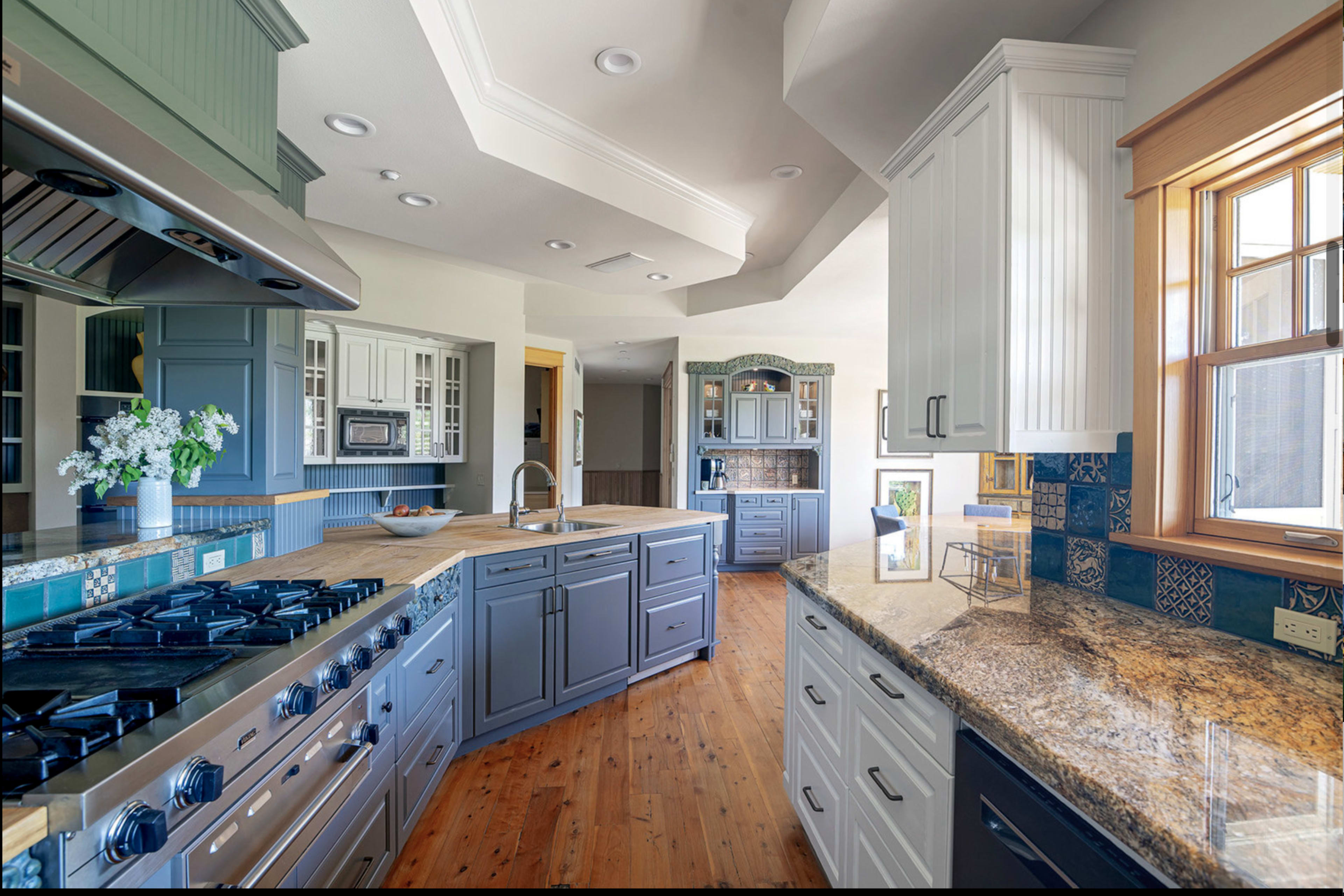 The kitchen features a spacious layout with a mix of blue and white cabinetry, granite countertops, and stainless steel appliances.
