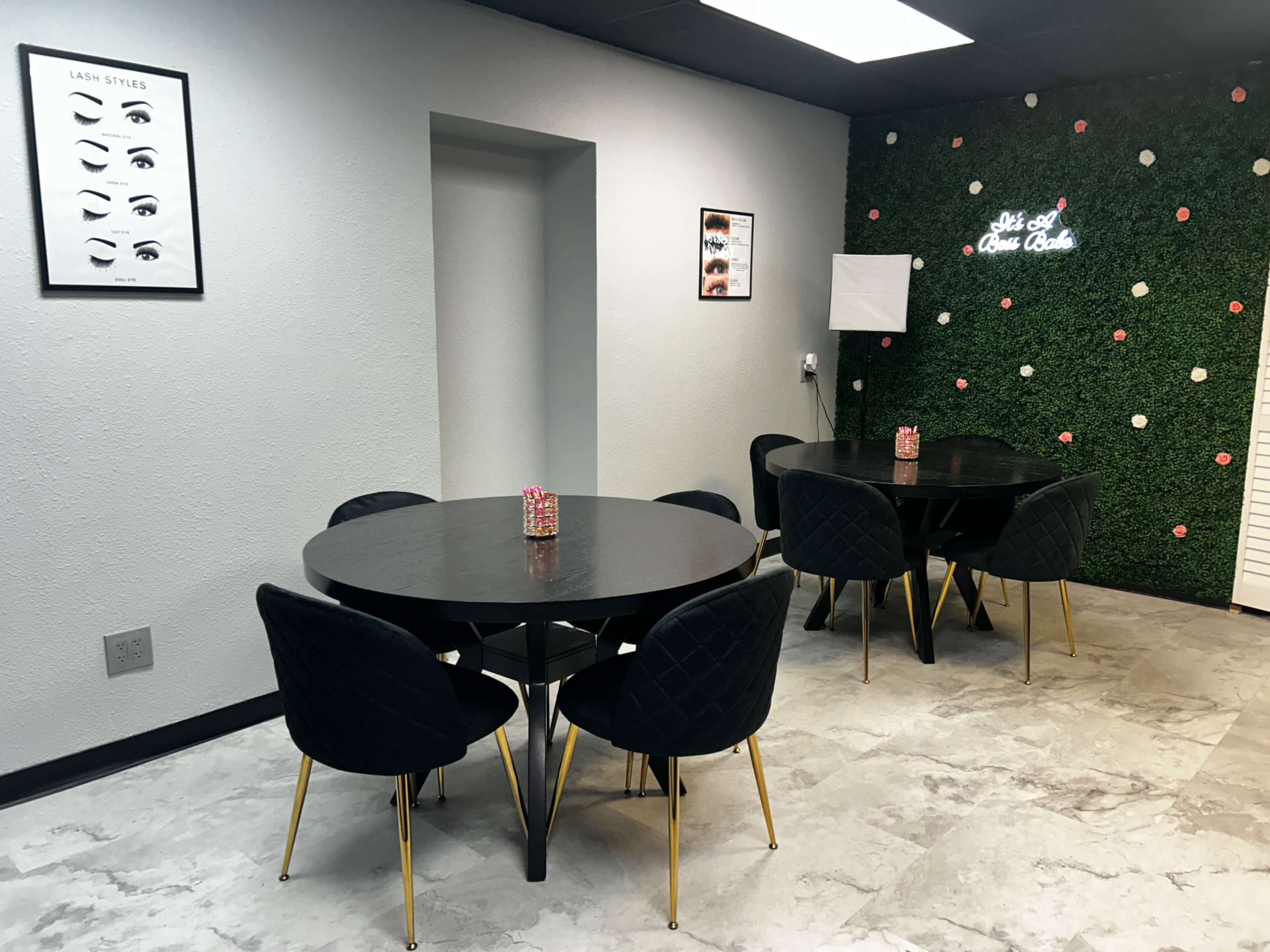 The image shows a modern interior space with two round black tables surrounded by black chairs, a green wall with decorative elements, and framed posters on the walls.