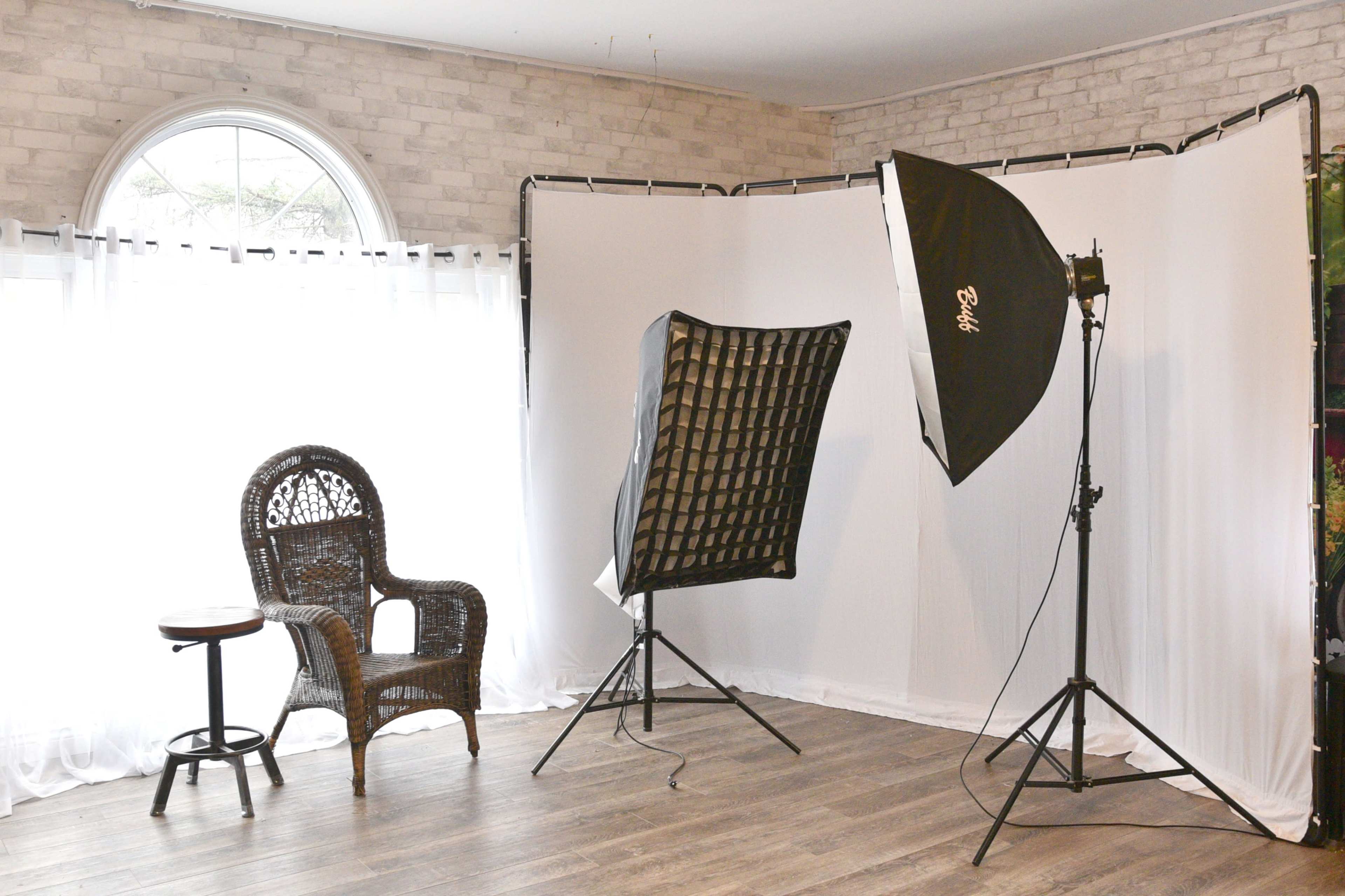 A photography studio features a wicker chair alongside a small table, with a backdrop and lighting setup.
