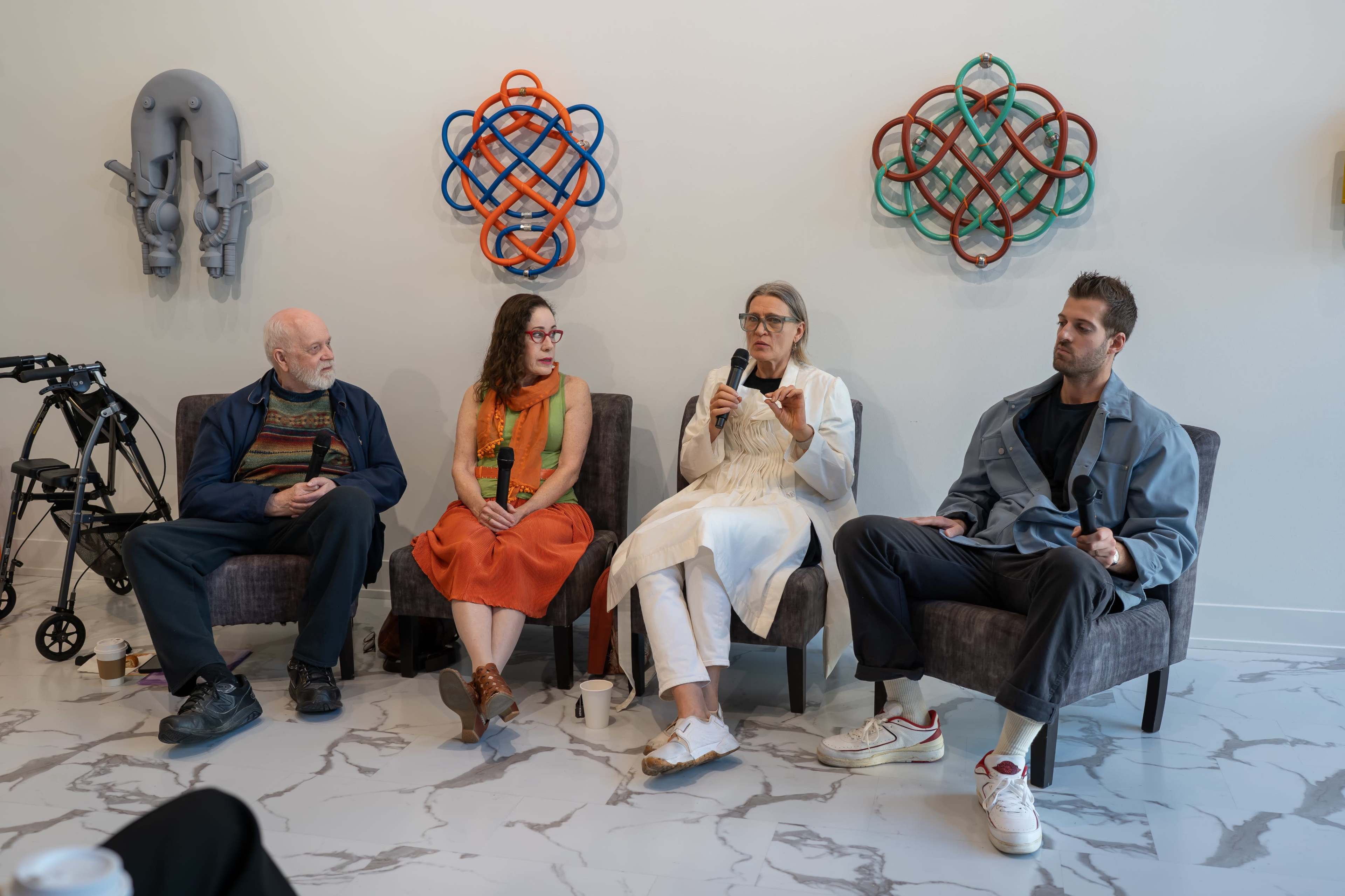 A panel discussion is taking place, featuring four individuals seated in modern chairs against a backdrop of colorful wall art.
