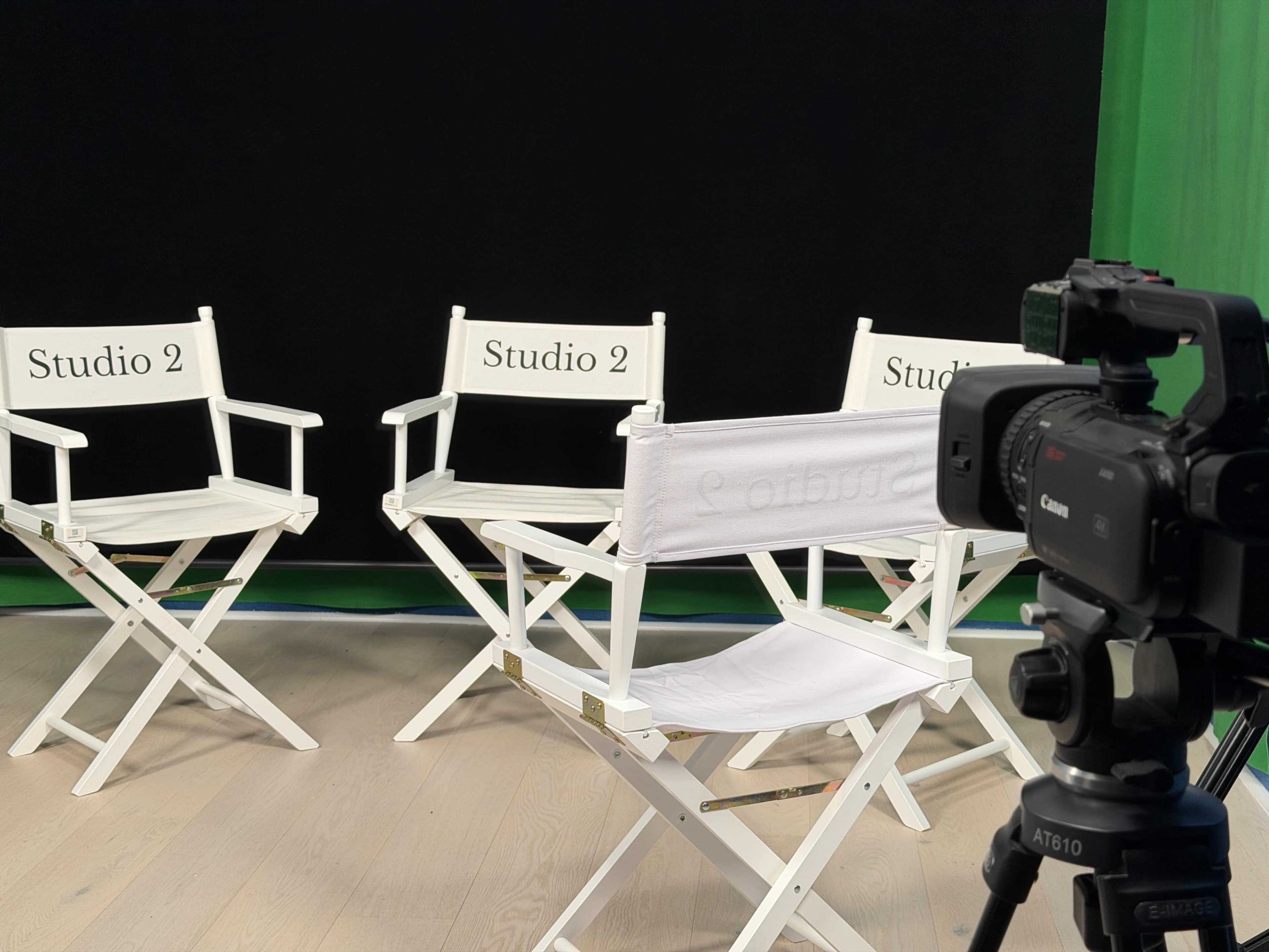 The image shows three white director's chairs labeled "Studio 2" arranged in front of a black backdrop, with a camera on a tripod positioned nearby.