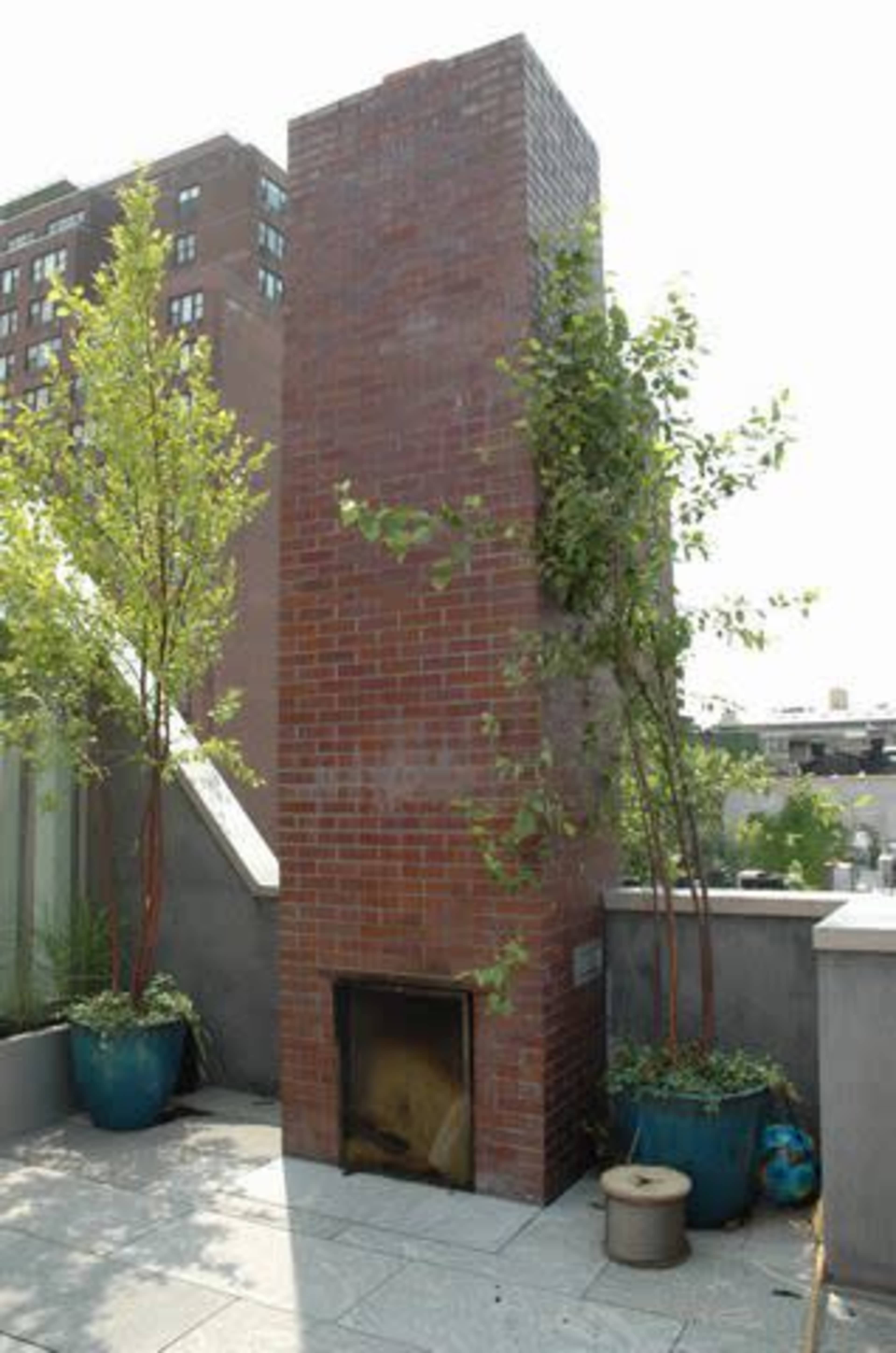 A brick outdoor chimney structure is surrounded by potted plants on a rooftop terrace.