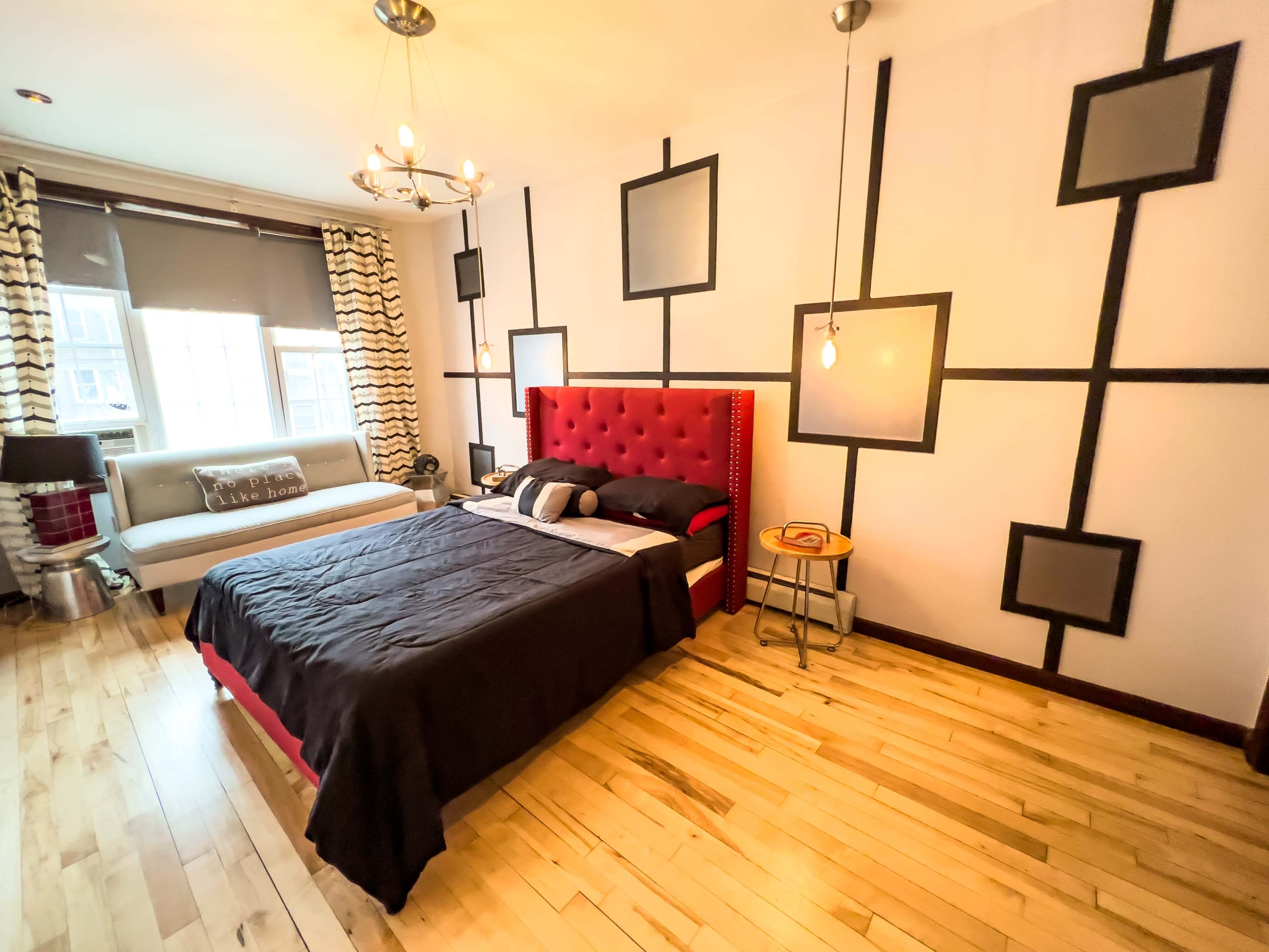 A modern bedroom featuring a red tufted headboard, a black bedspread, a sofa, and geometric wall decorations.