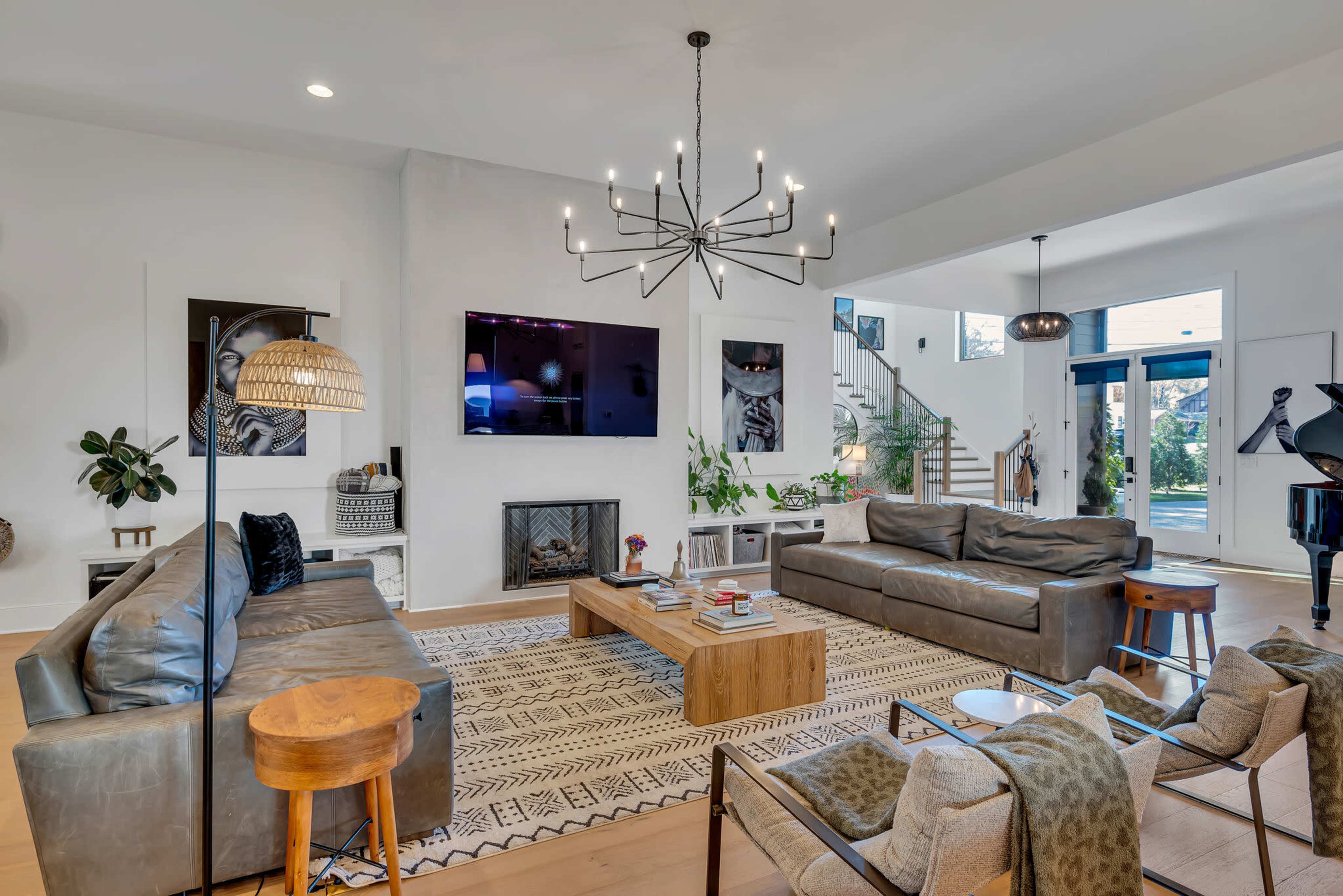 A modern living room features two leather sofas facing a wooden coffee table, a television mounted on the wall, and a staircase in the background.