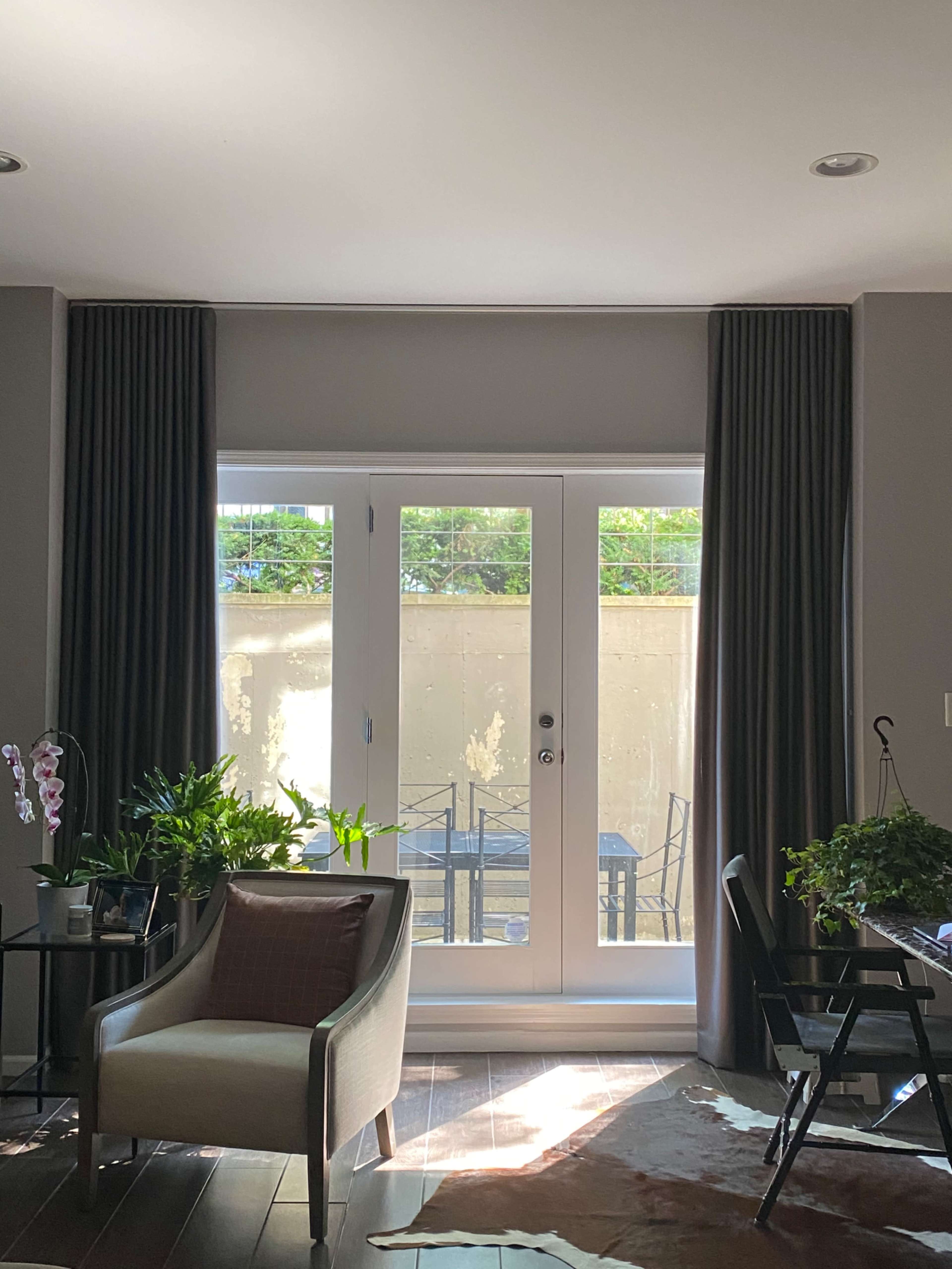 A modern living room features a chair, plants, and a glass door opening to a patio with a table and chairs.