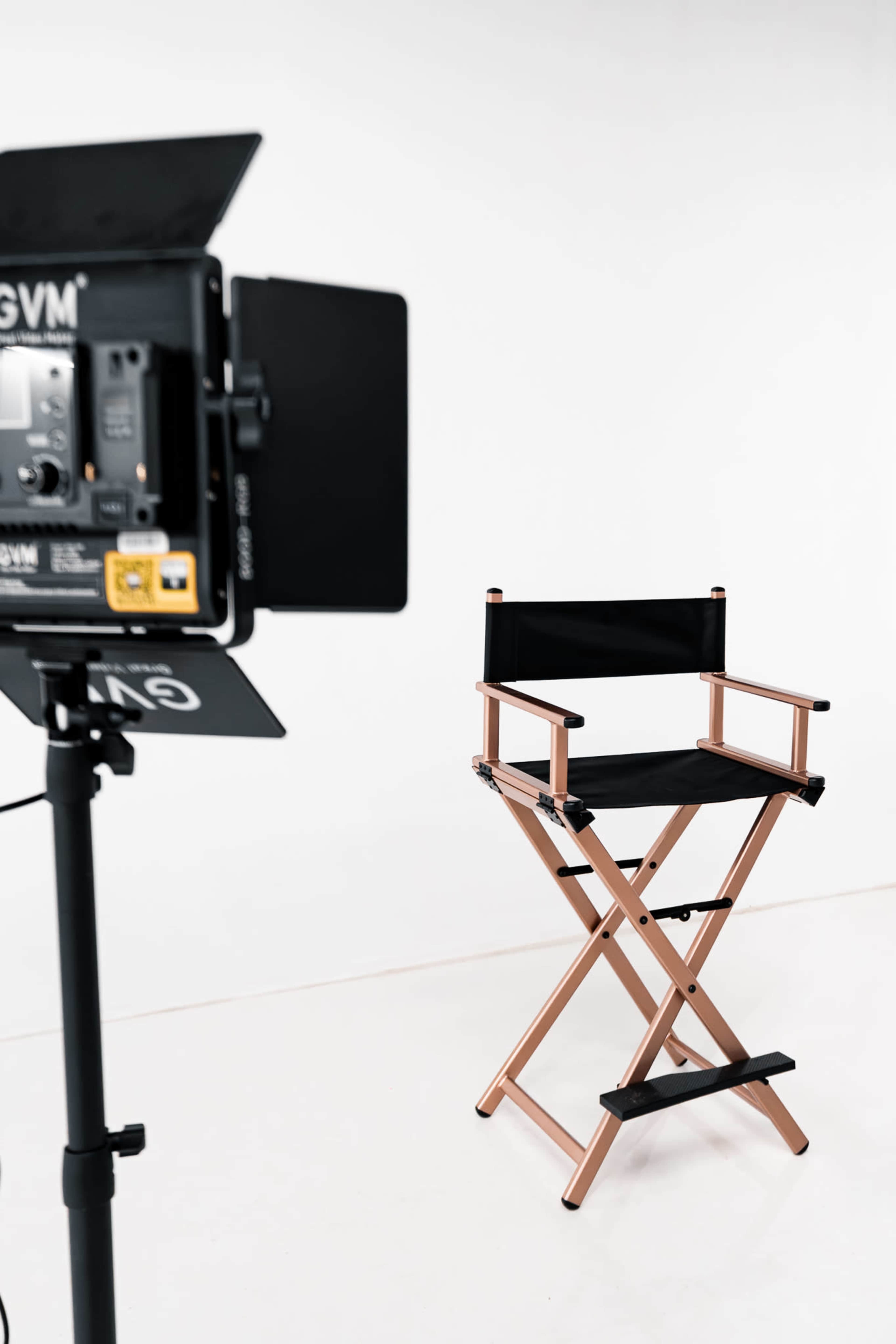 A director's chair is positioned in front of a mounted light and backdrop in a minimalist studio setting.