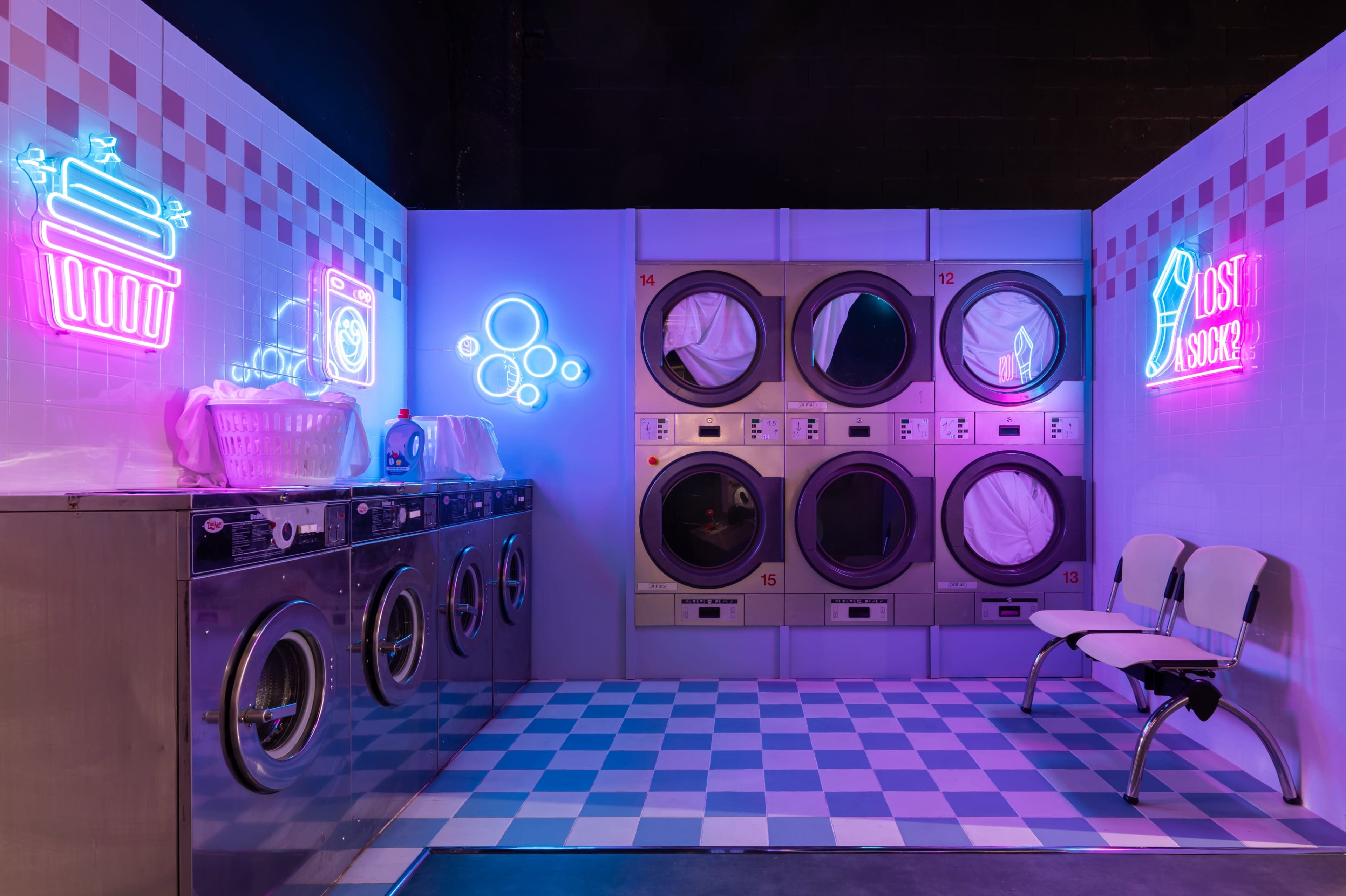 The image shows a laundromat with several washing machines and dryers, complemented by neon signs and a checkered floor.