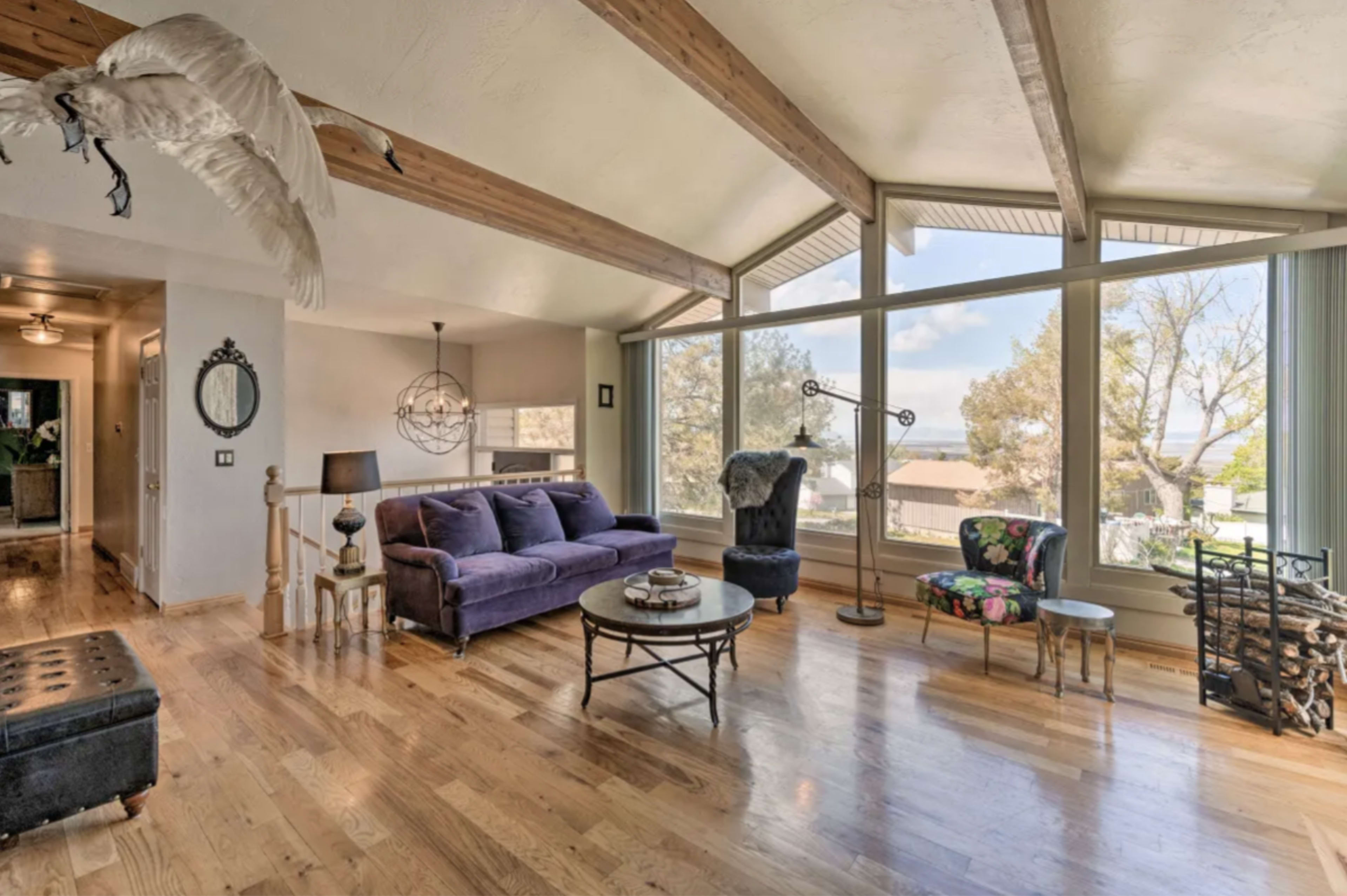 A spacious living room with a vaulted ceiling, large windows, and a mix of seating arrangements including a purple couch and a patterned chair.