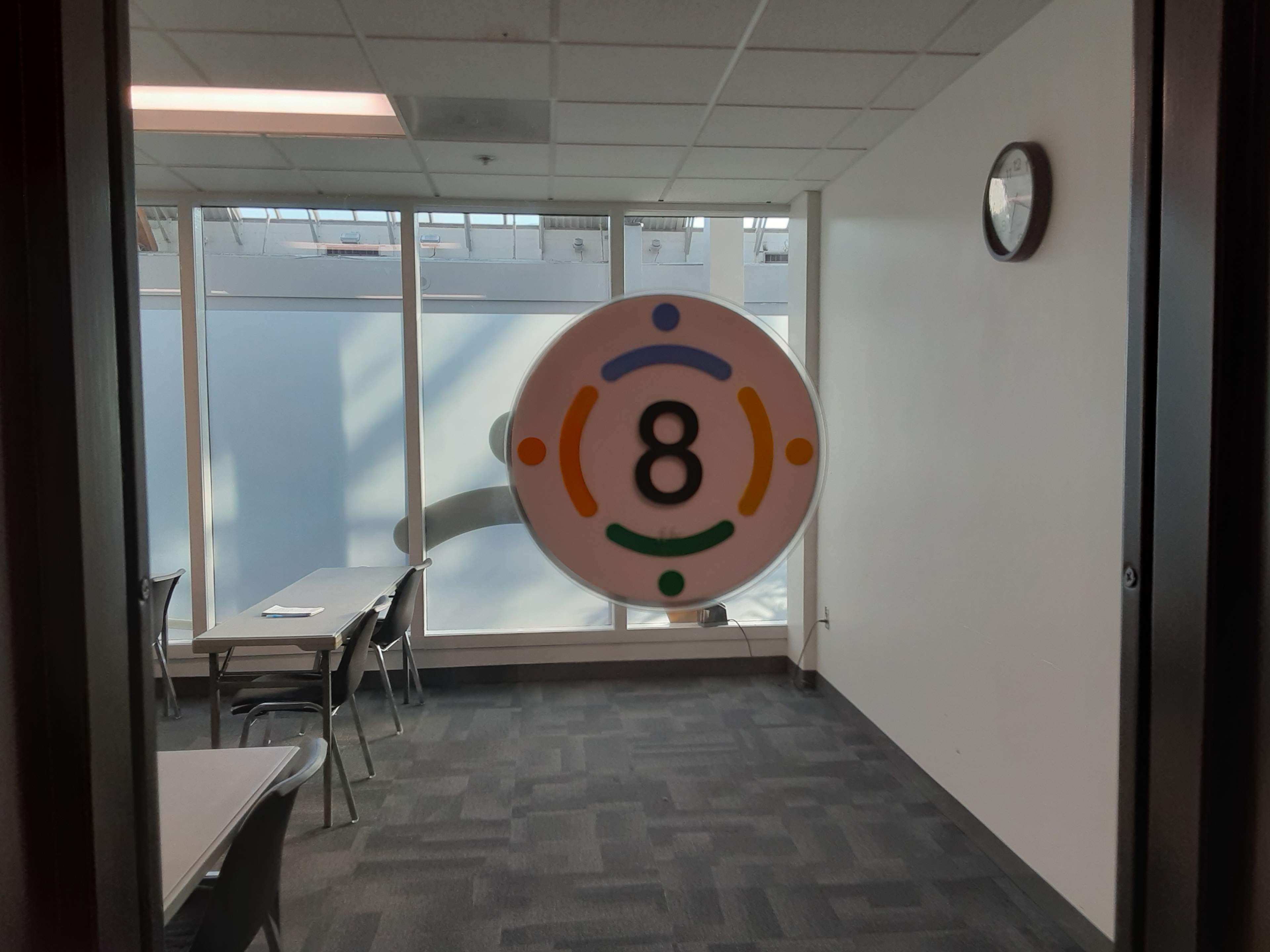 A door displays a circular sign with the number "8" and colored circles around it, leading to a well-lit room with tables and chairs.