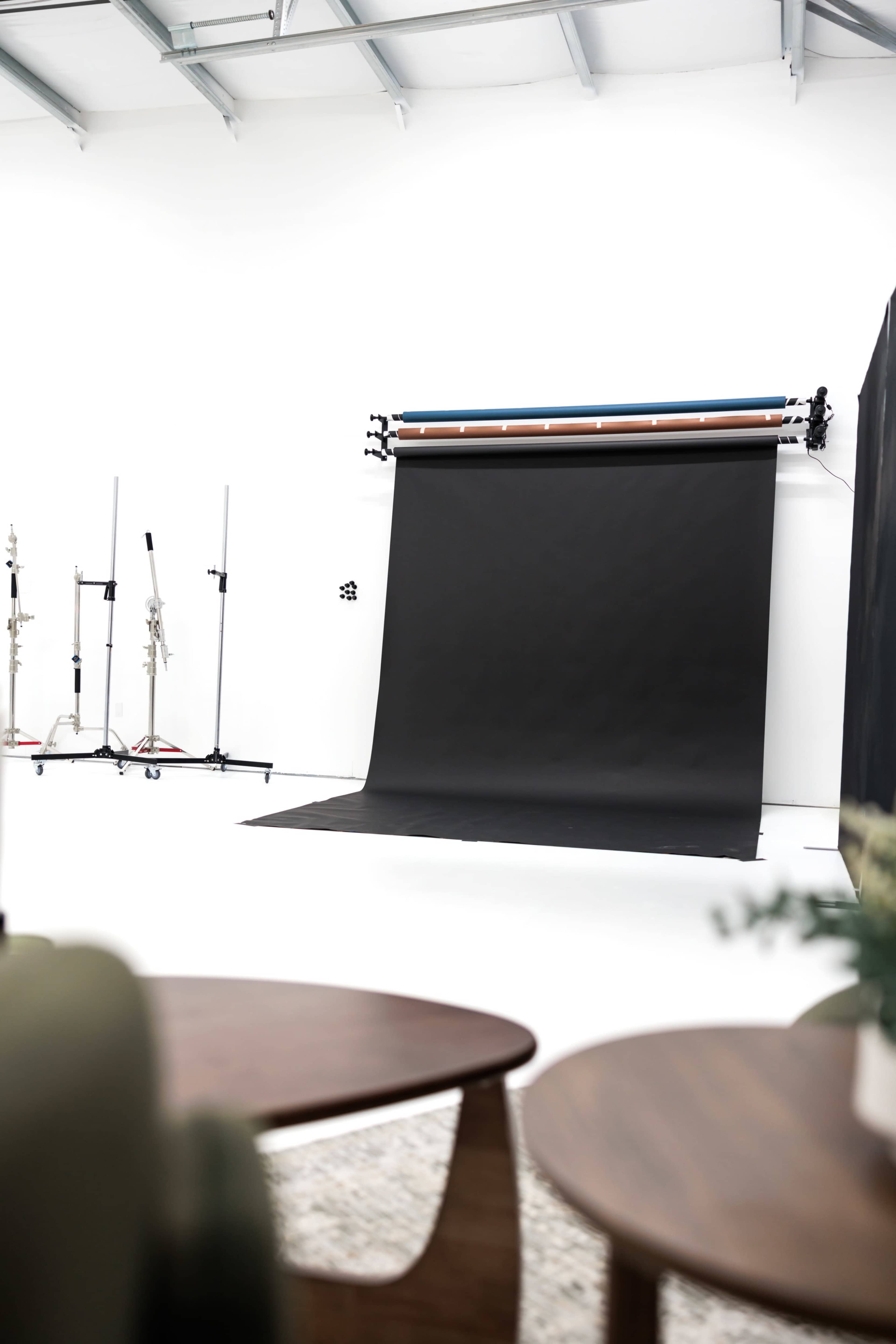The image shows a photography studio with a black backdrop and two wooden tables in the foreground.