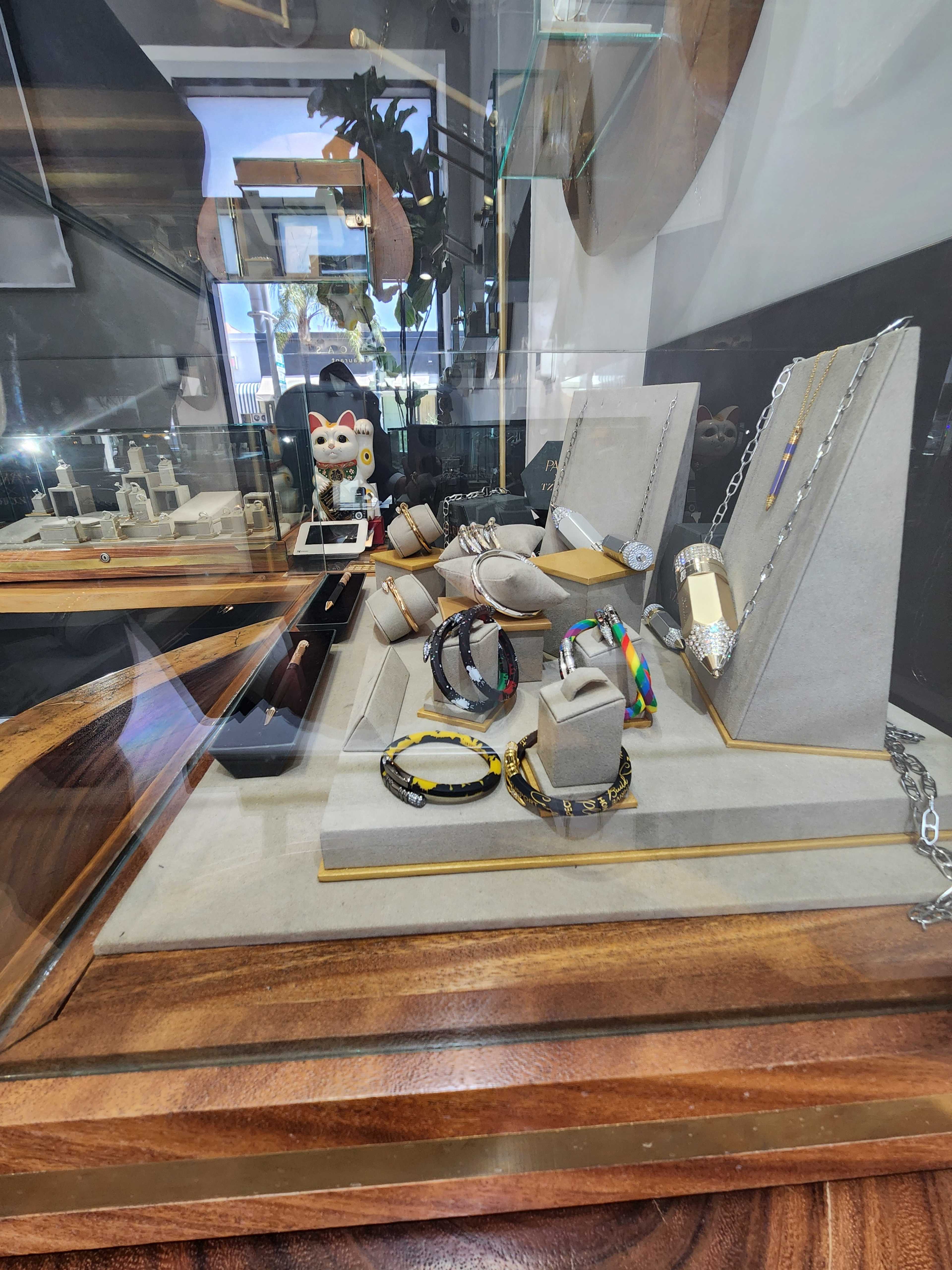 The image shows a display case featuring various pieces of jewelry, including rings, bracelets, and necklaces, arranged on gray stands.