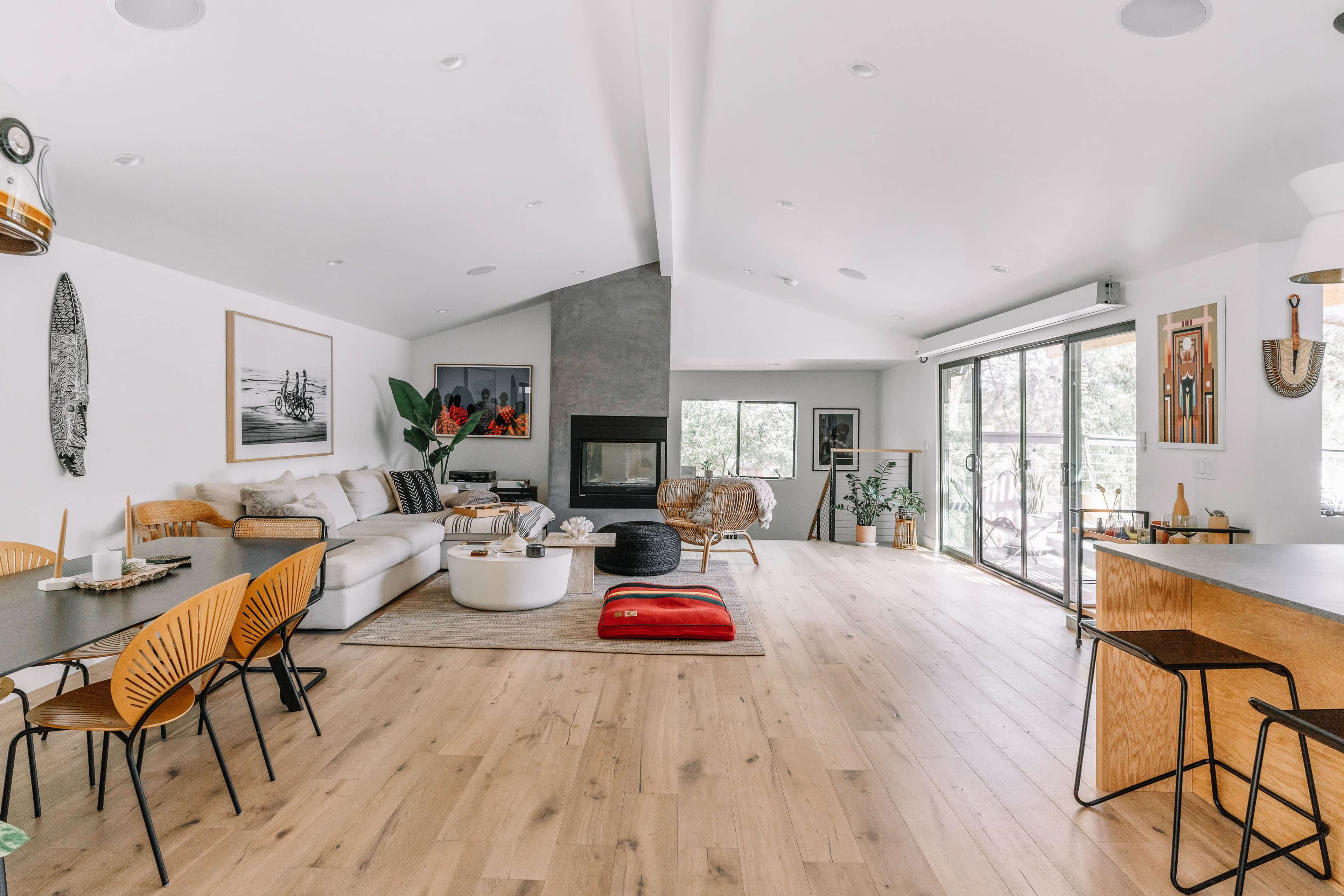 The image depicts a modern open-concept living space featuring a seating area with a light-colored sofa, a dining area with black chairs, and large windows allowing natural light.