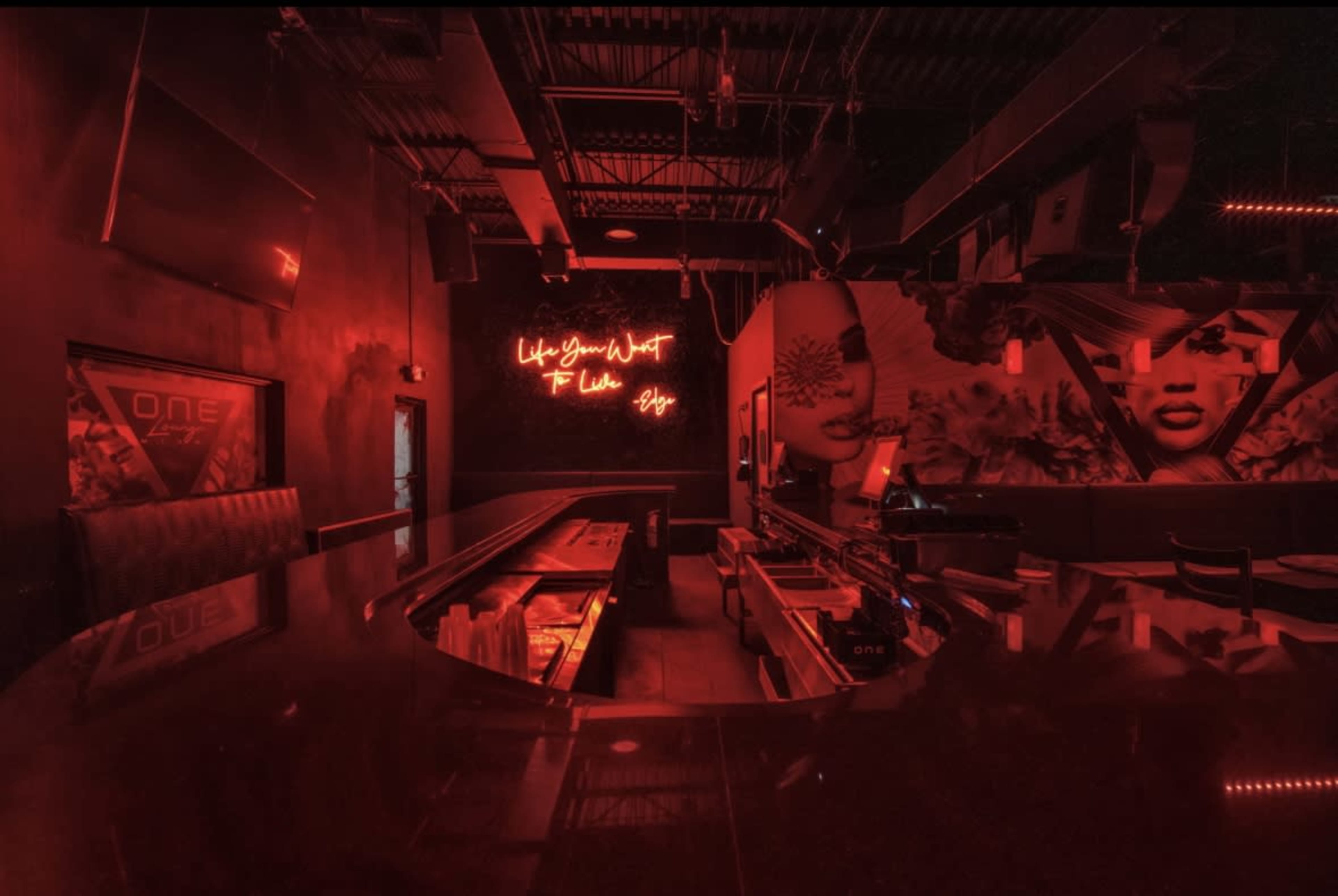 The image shows a dimly-lit bar interior featuring a curved counter, neon signage, and vibrant wall murals.