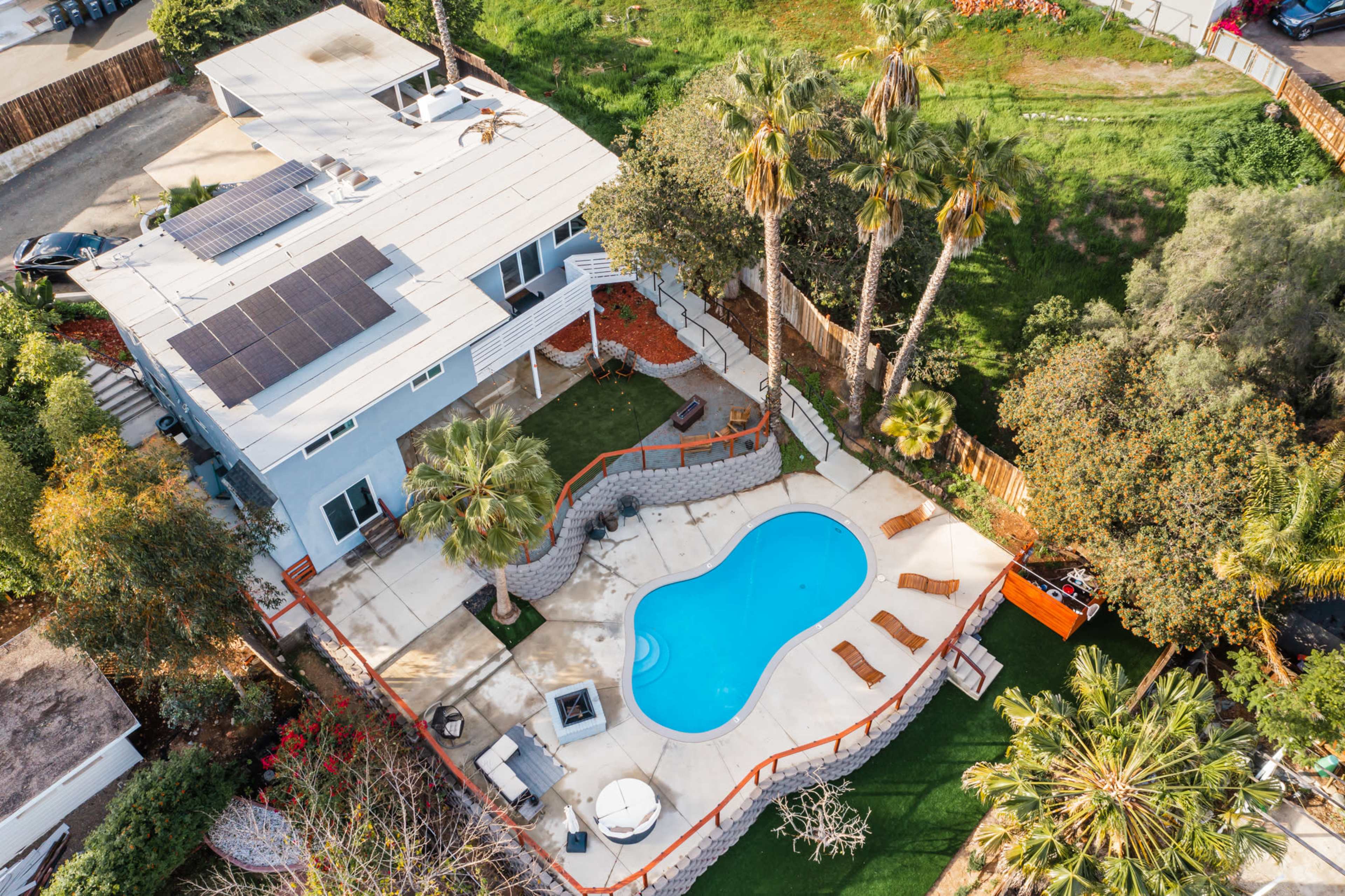 An aerial view of a residential property featuring a swimming pool surrounded by palm trees and an outdoor seating area.