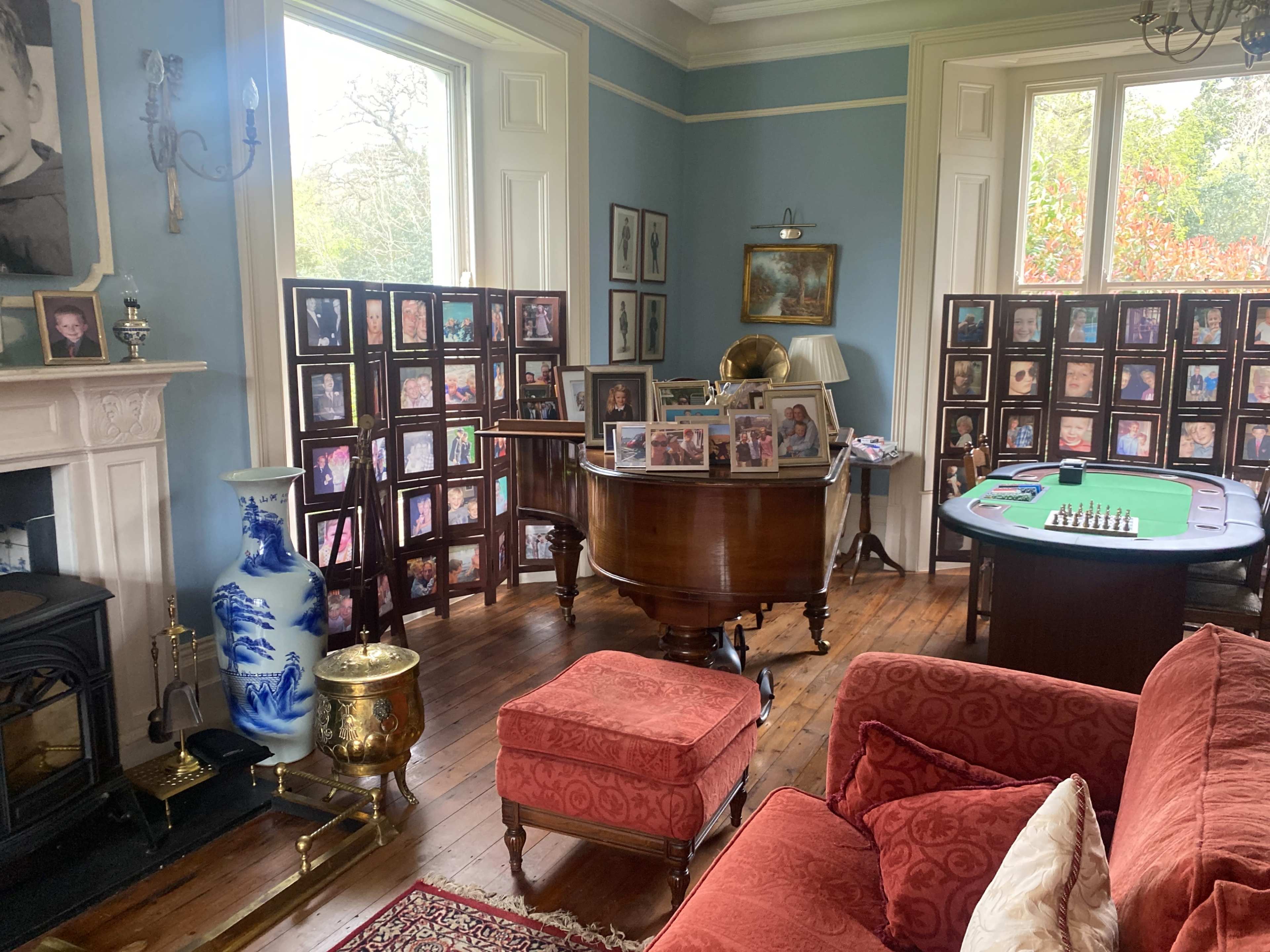 A room with a grand piano, framed photographs on display, a poker table, and a red couch.