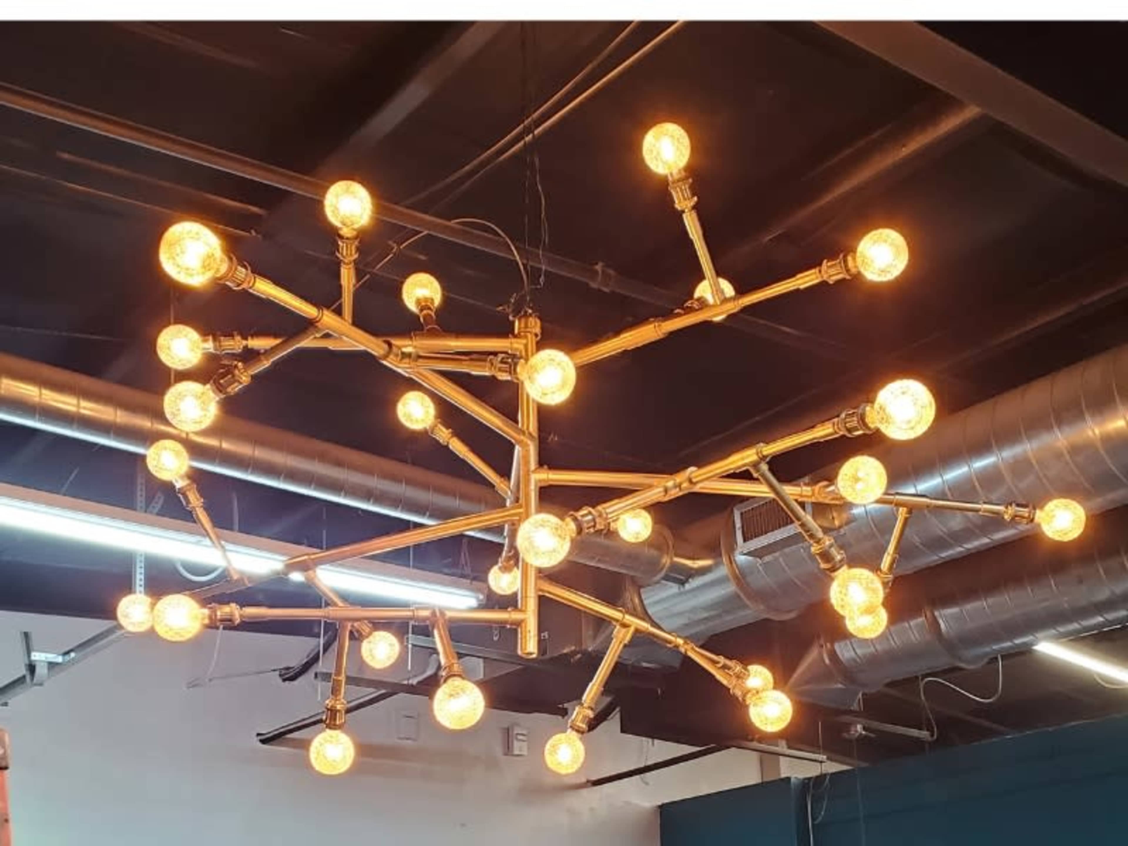A large, industrial-style chandelier with multiple light bulbs arranged in a branching pattern hangs from a ceiling.