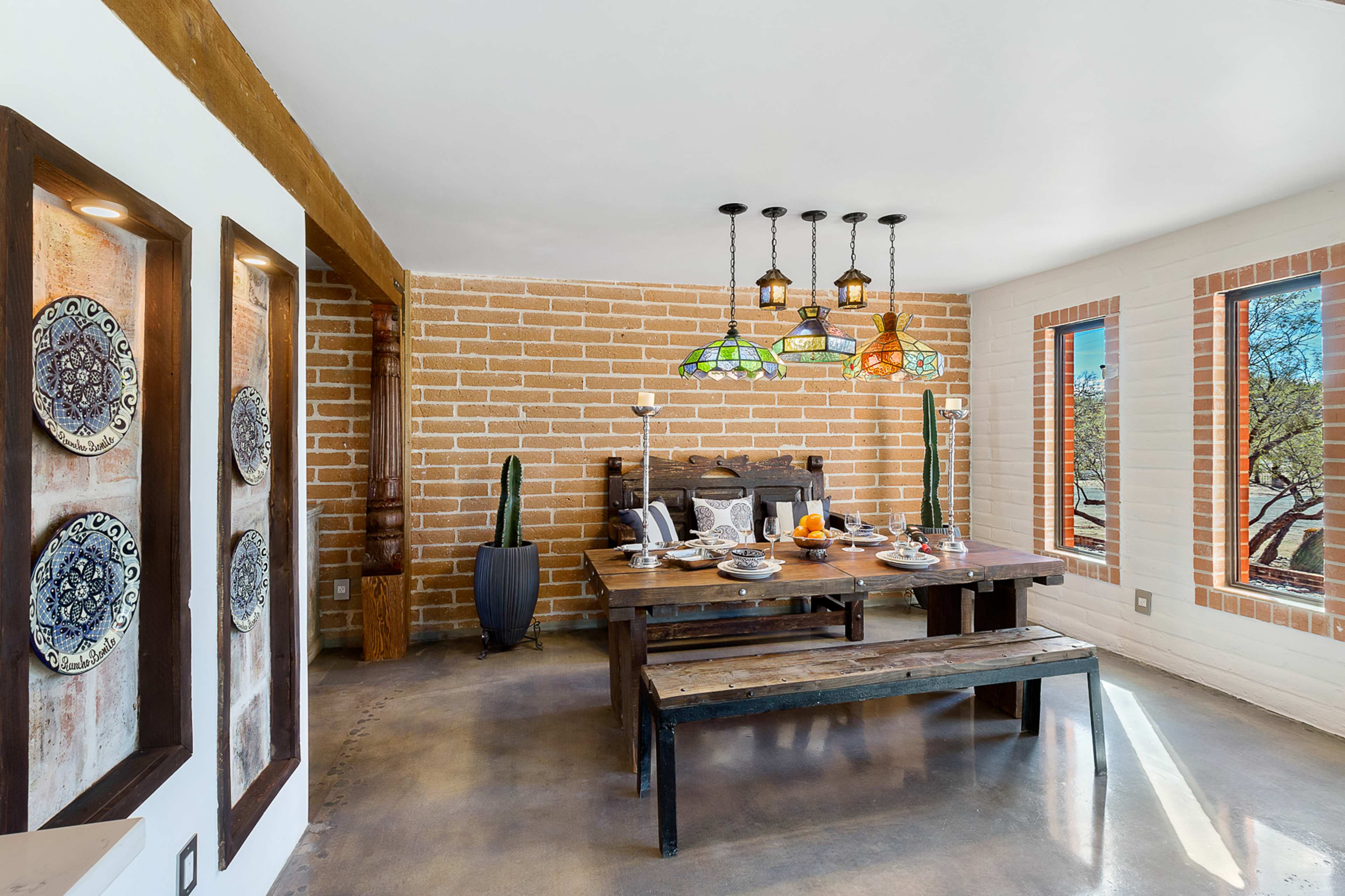 A dining area with a wooden table set for a meal, surrounded by colorful stained glass lights and brick walls.