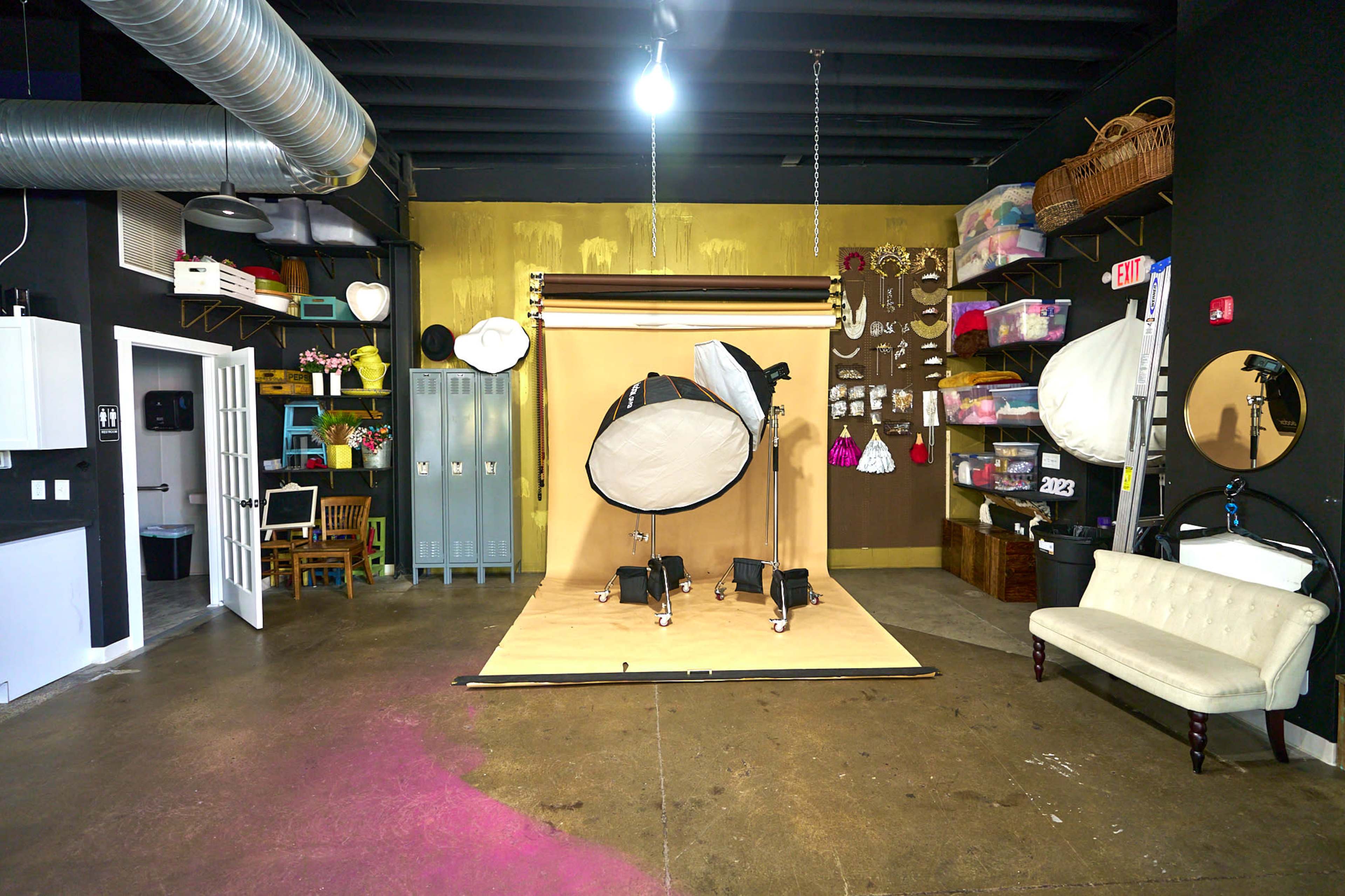 A photography studio with a backdrop setup, various lighting equipment, and organized storage on the walls.