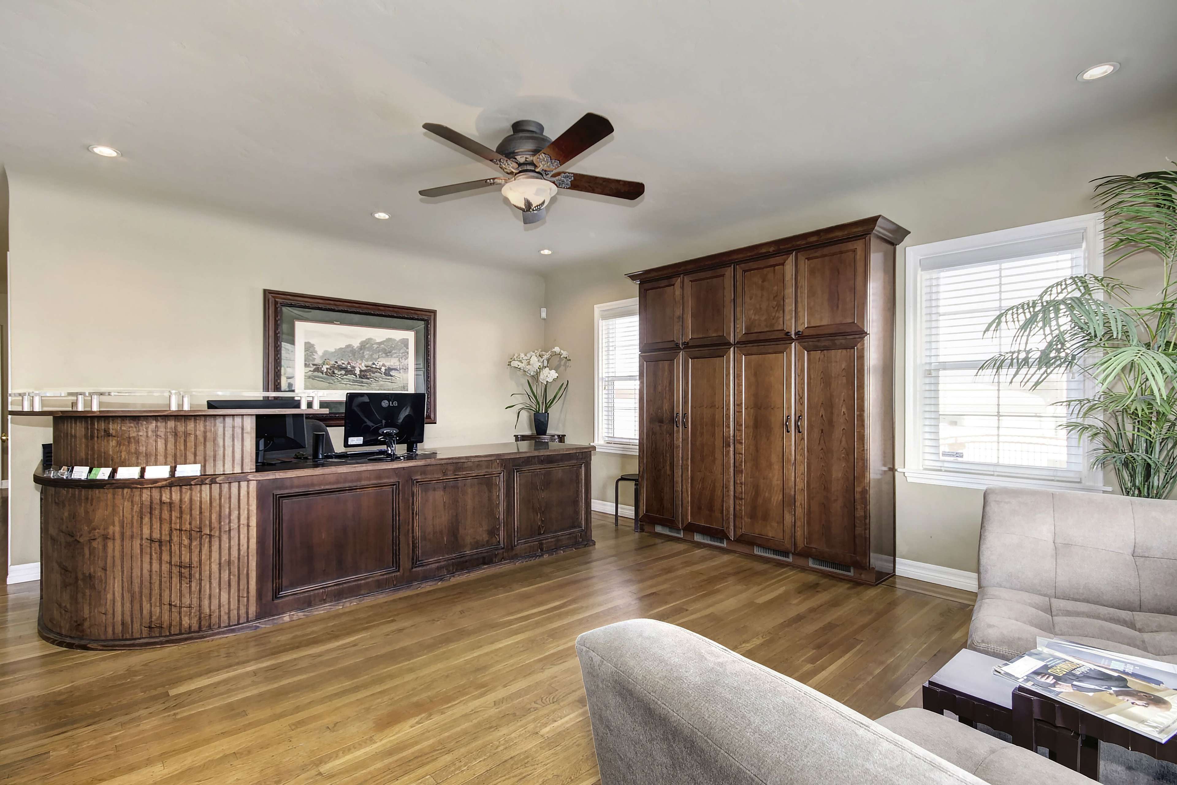 A reception area with a wooden front desk, a large cabinet, and seating arranged around a coffee table.