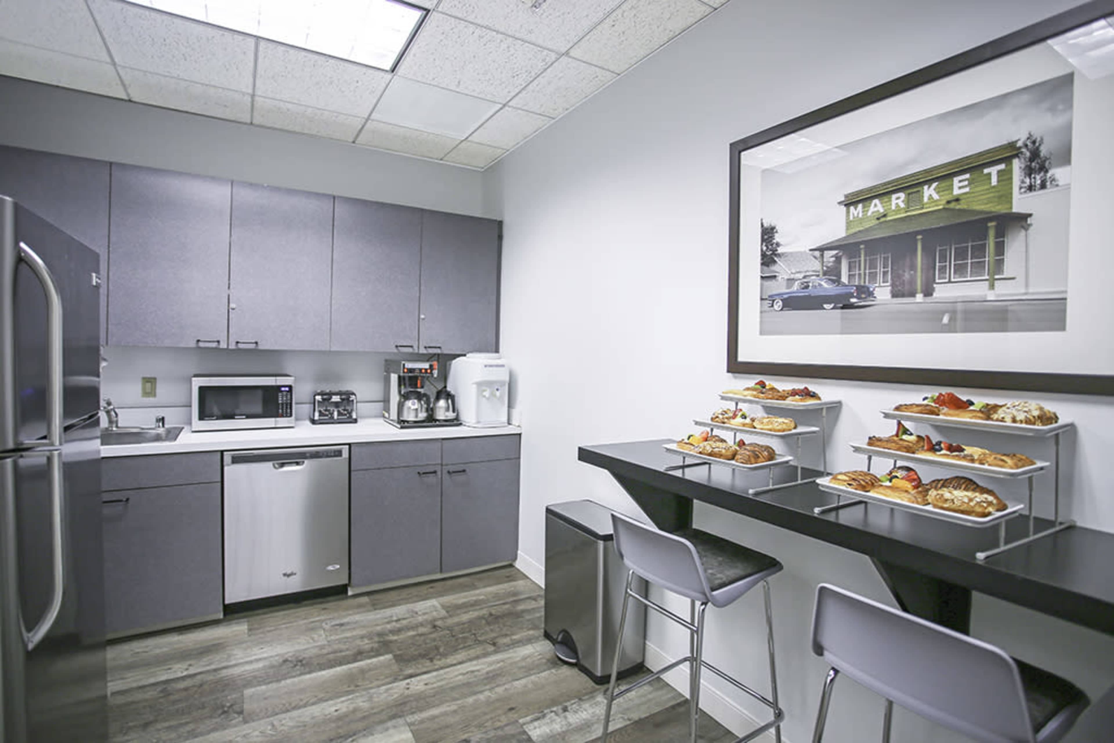 A modern kitchen area with gray cabinets, a stainless steel refrigerator, and a table displaying a variety of food items.