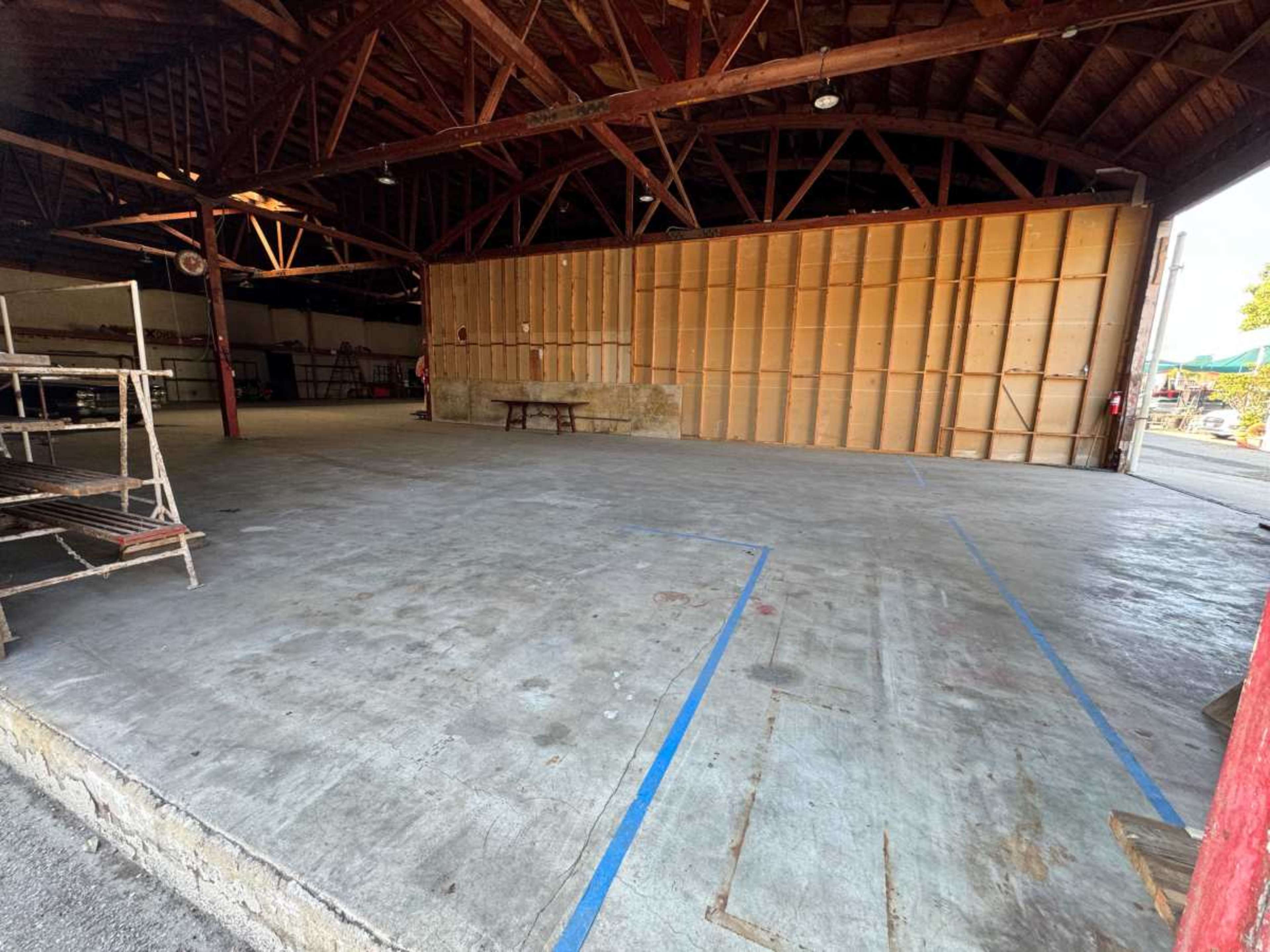 The image shows an empty industrial space with wooden beams and a concrete floor, featuring a large wall with wooden panels on one side.