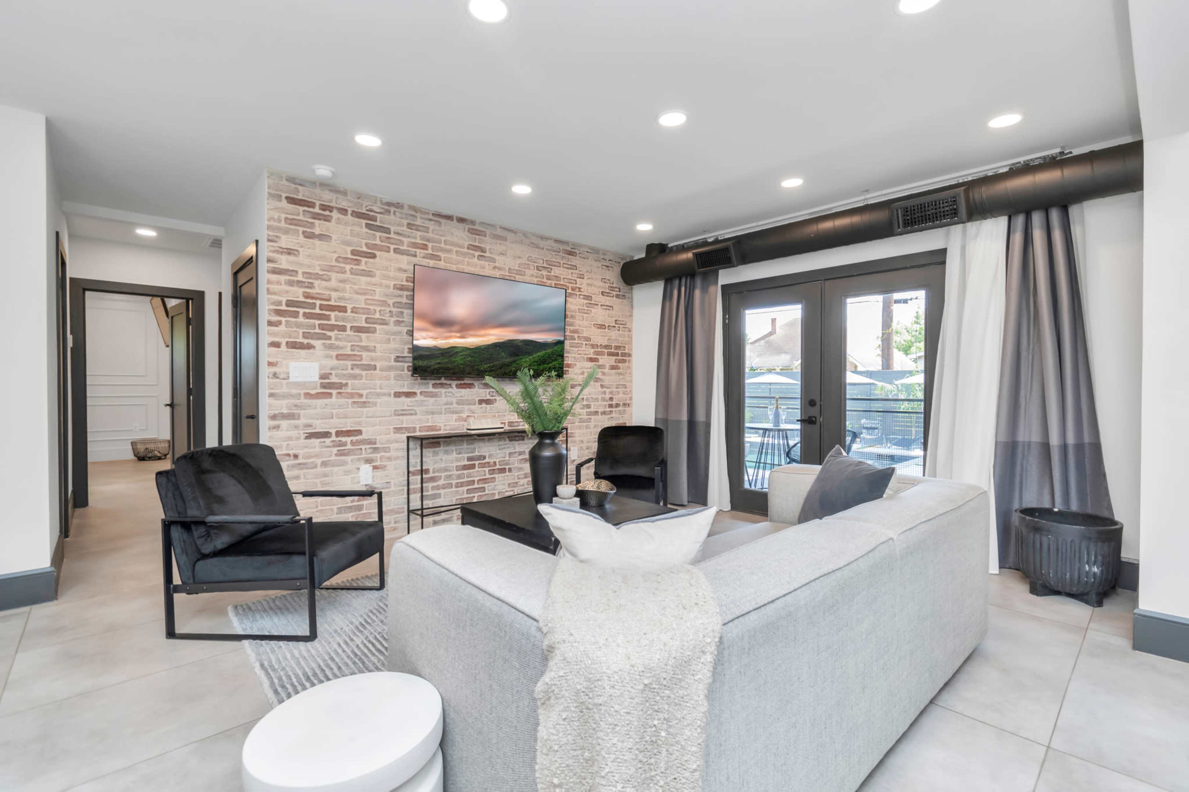 The living room features a brick accent wall, modern furniture, and large windows leading to a balcony.