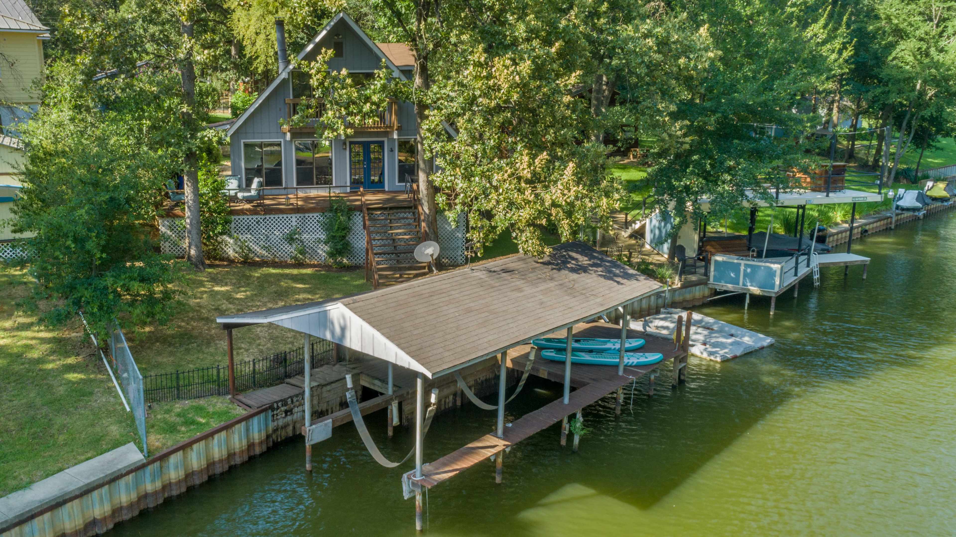 A waterfront property with a dock, two kayaks, and a house surrounded by trees.