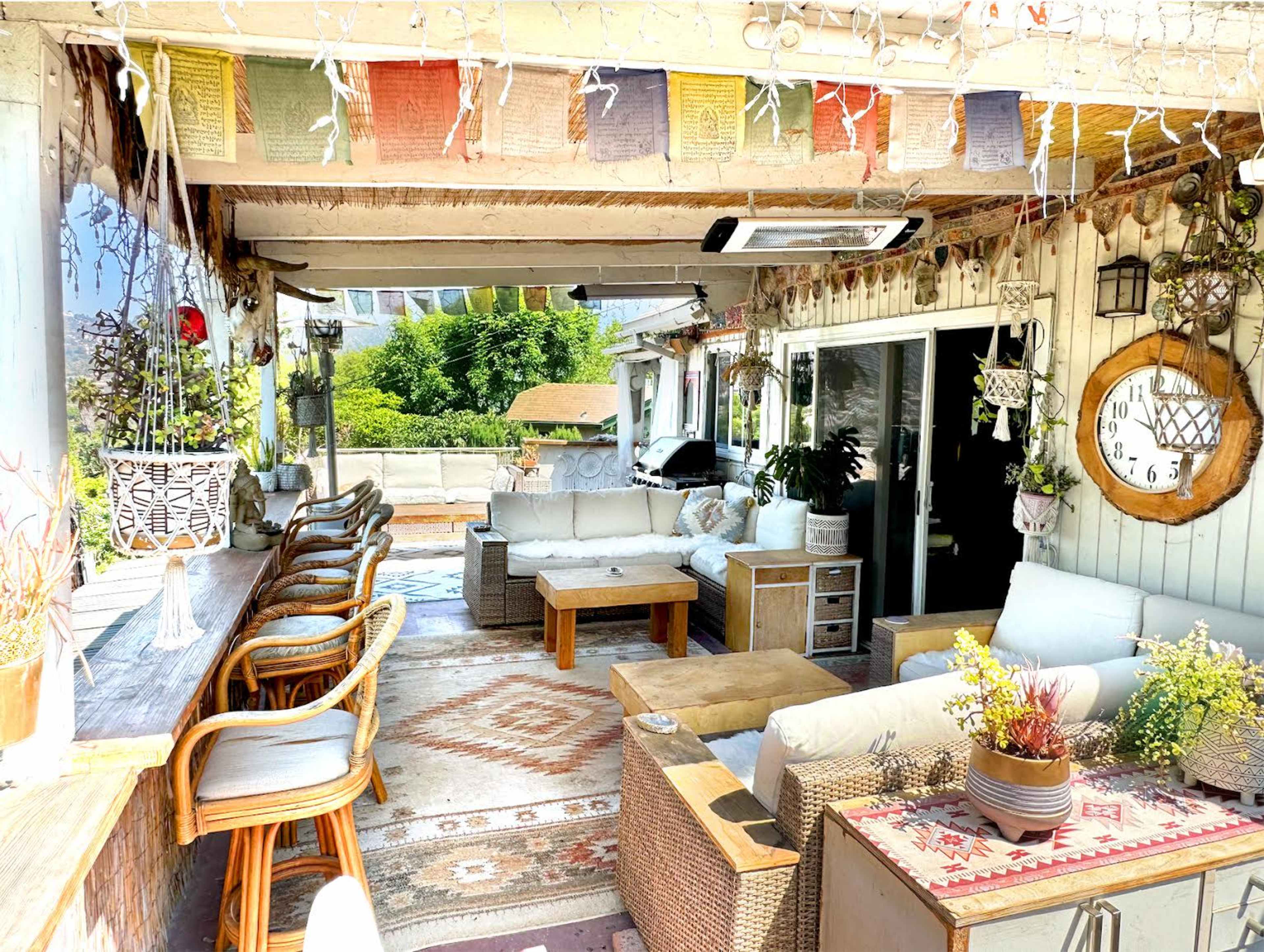 A spacious, covered outdoor lounge area furnished with sofas, a wooden coffee table, and decorative elements such as plants and fairy lights.
