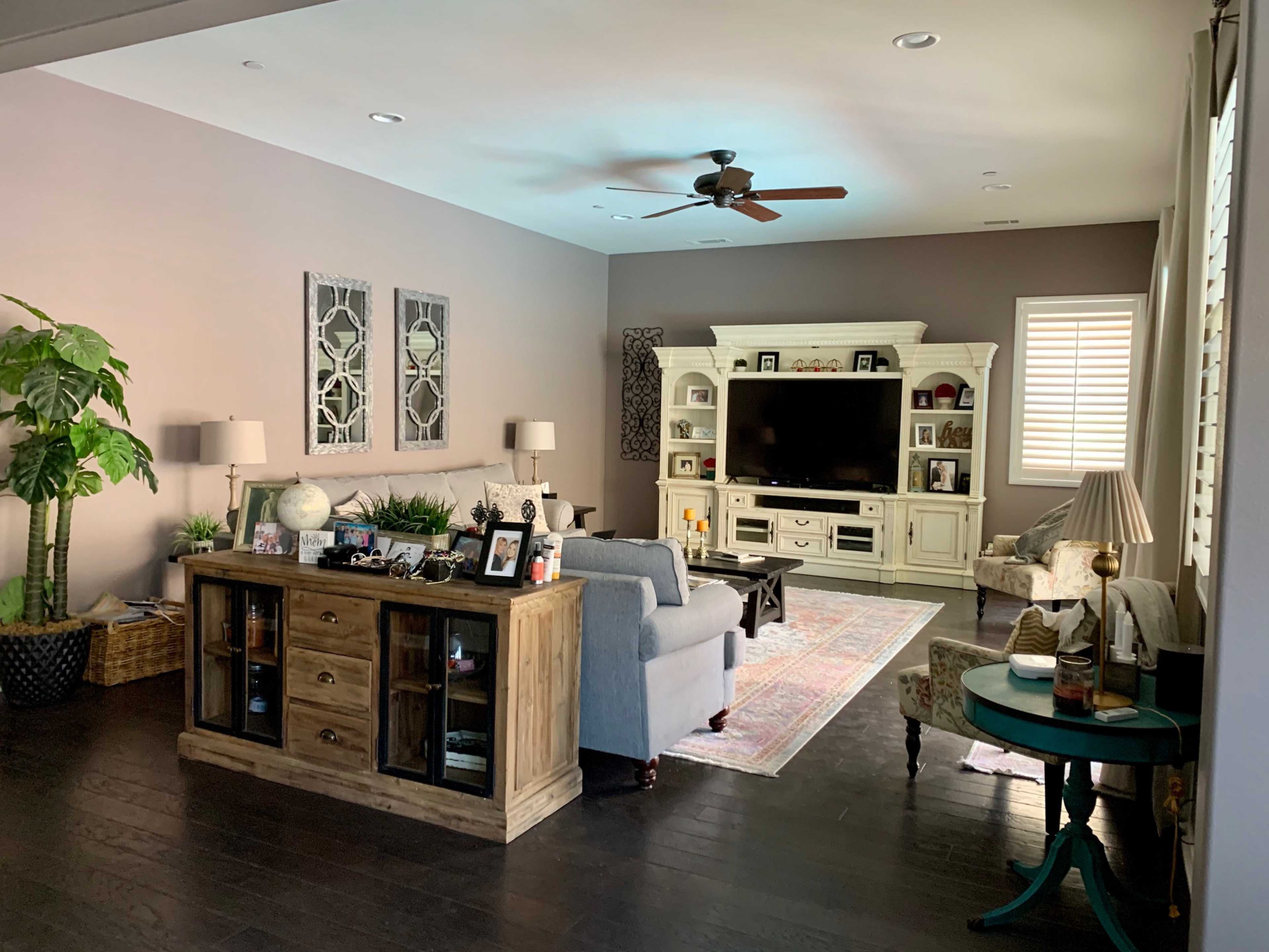 A modern living room with a light-colored wall, dark wooden flooring, a large entertainment center, and various furniture including a grey sofa and a green side table.