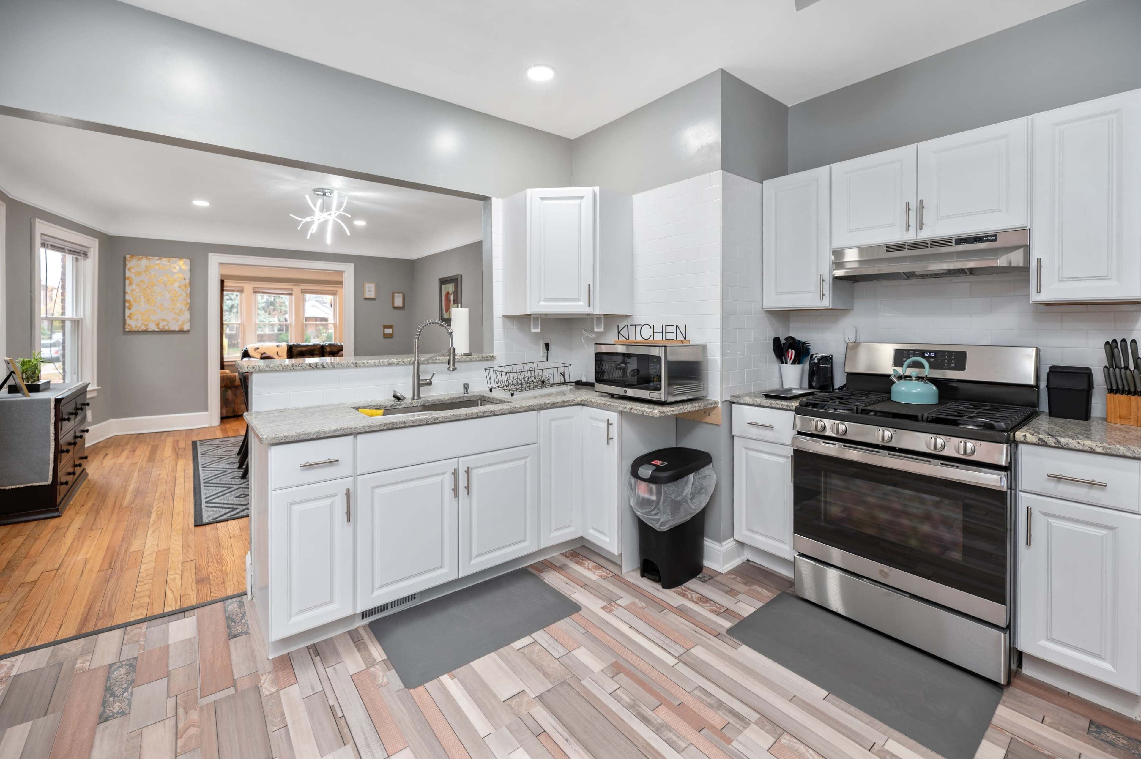 A modern kitchen with white cabinetry, stainless steel appliances, and a granite countertop, overlooking a living area through an open layout.