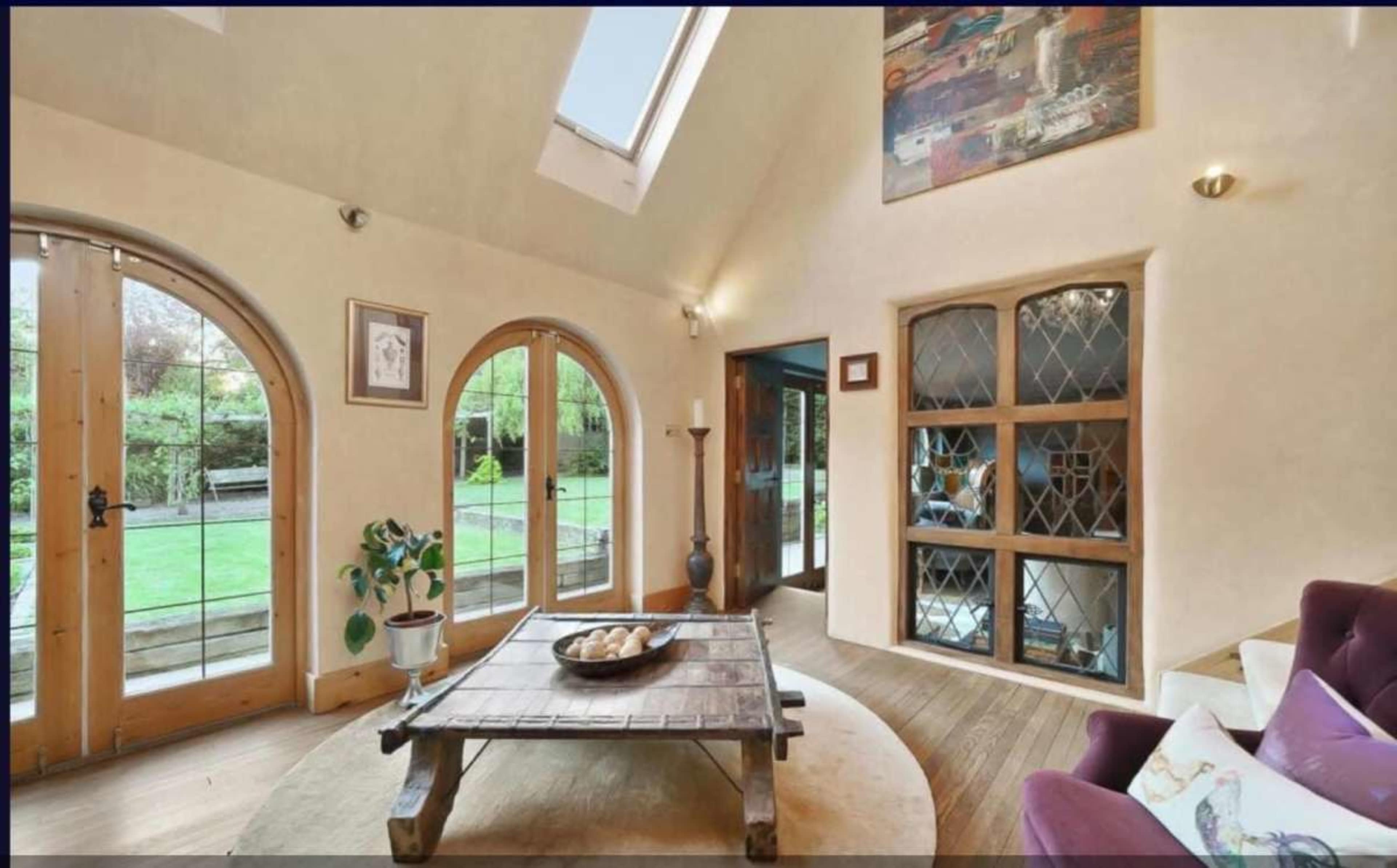The interior of a cozy living room features arched wooden doors, a coffee table in the center, and a large window with natural light illuminating the space.
