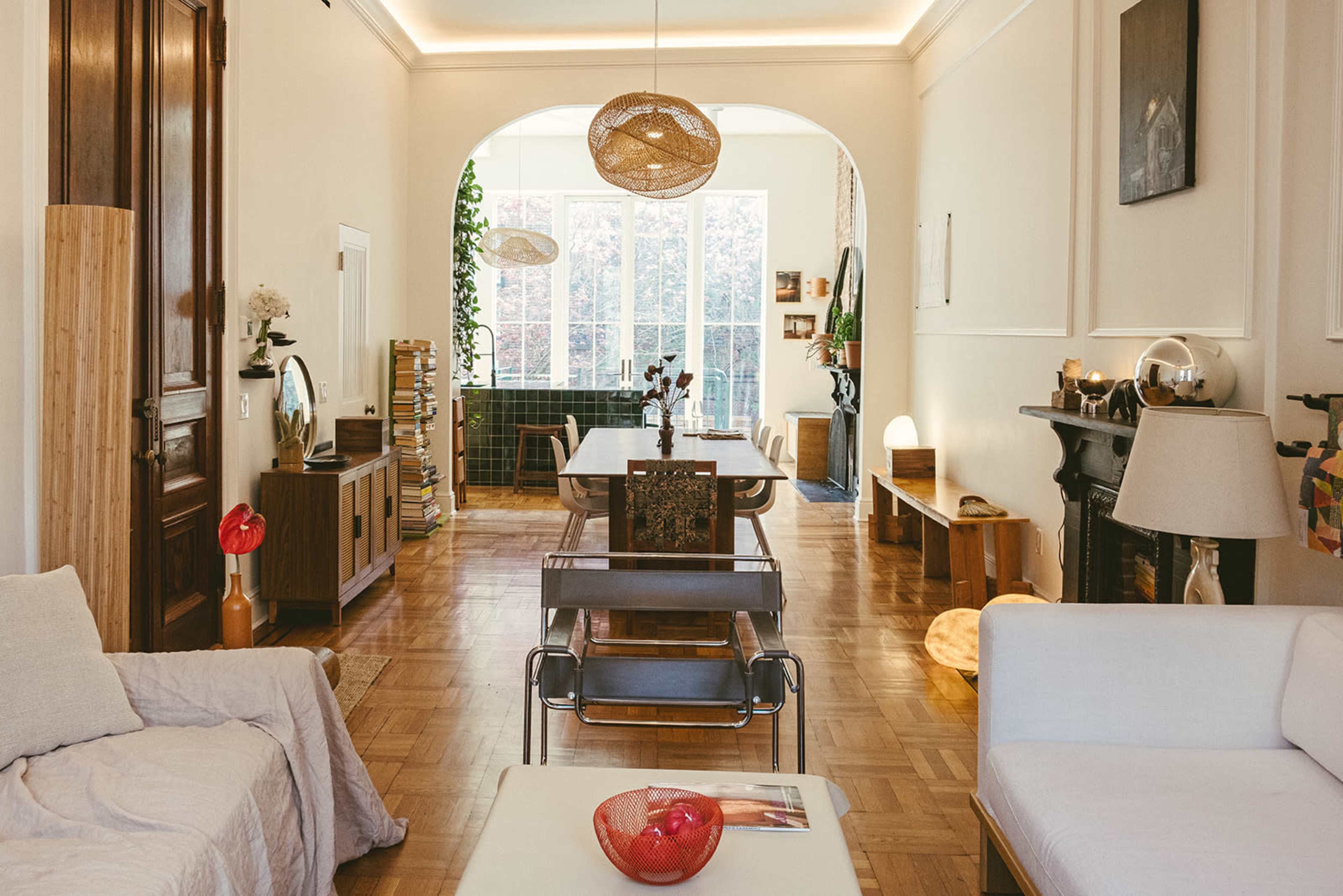 The image shows a spacious living room with a mix of modern and vintage furniture, featuring large windows that allow natural light to fill the space.