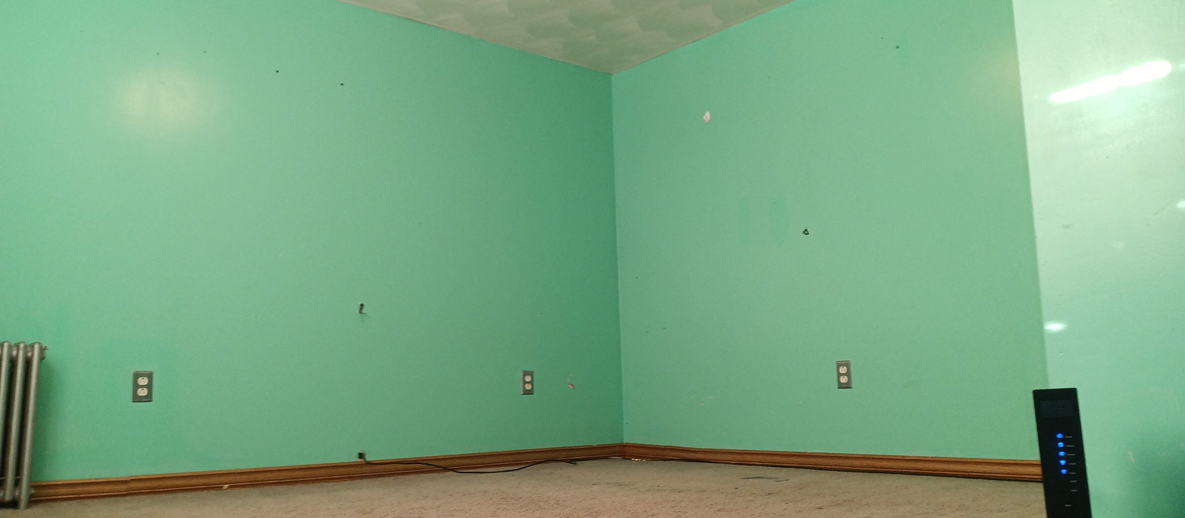 An empty room with turquoise walls, a carpeted floor, and visible electrical outlets.