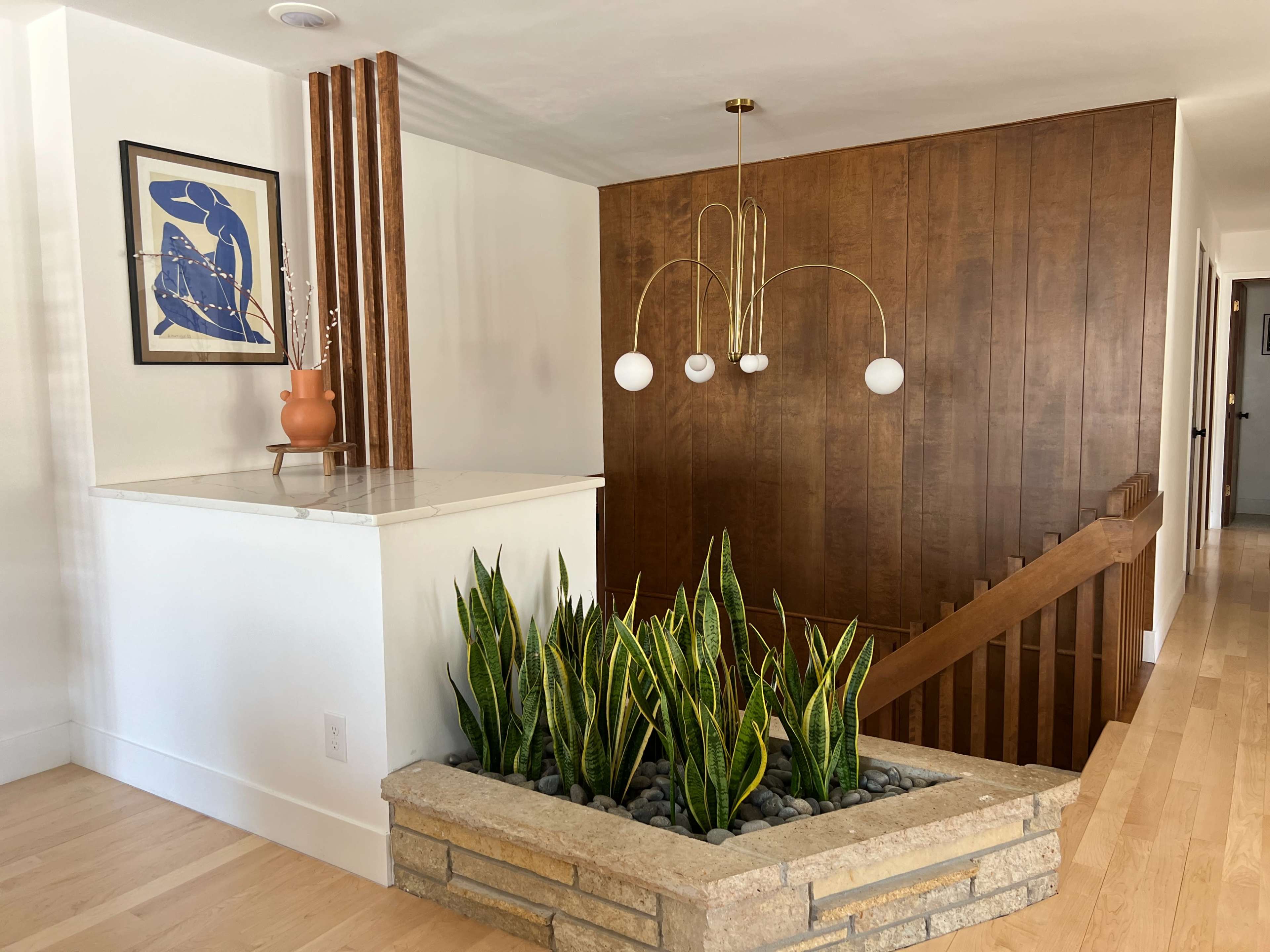 A modern interior featuring a wooden accent wall, a stairway, a decorative planter with snake plants, and a pendant light with three white globes.