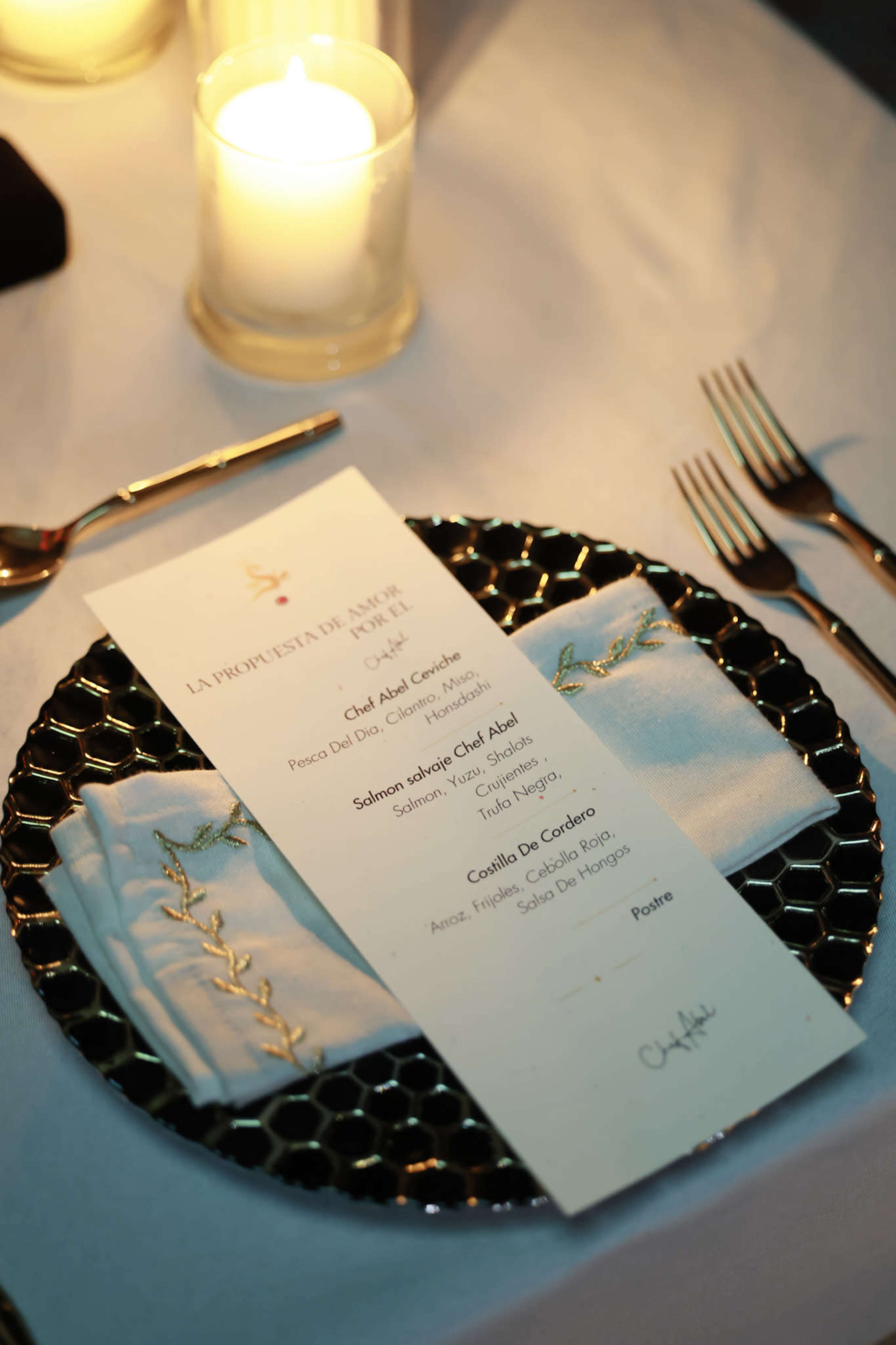 A formal dinner plate is set on a table with a menu, decorative napkin, and candles in the background.