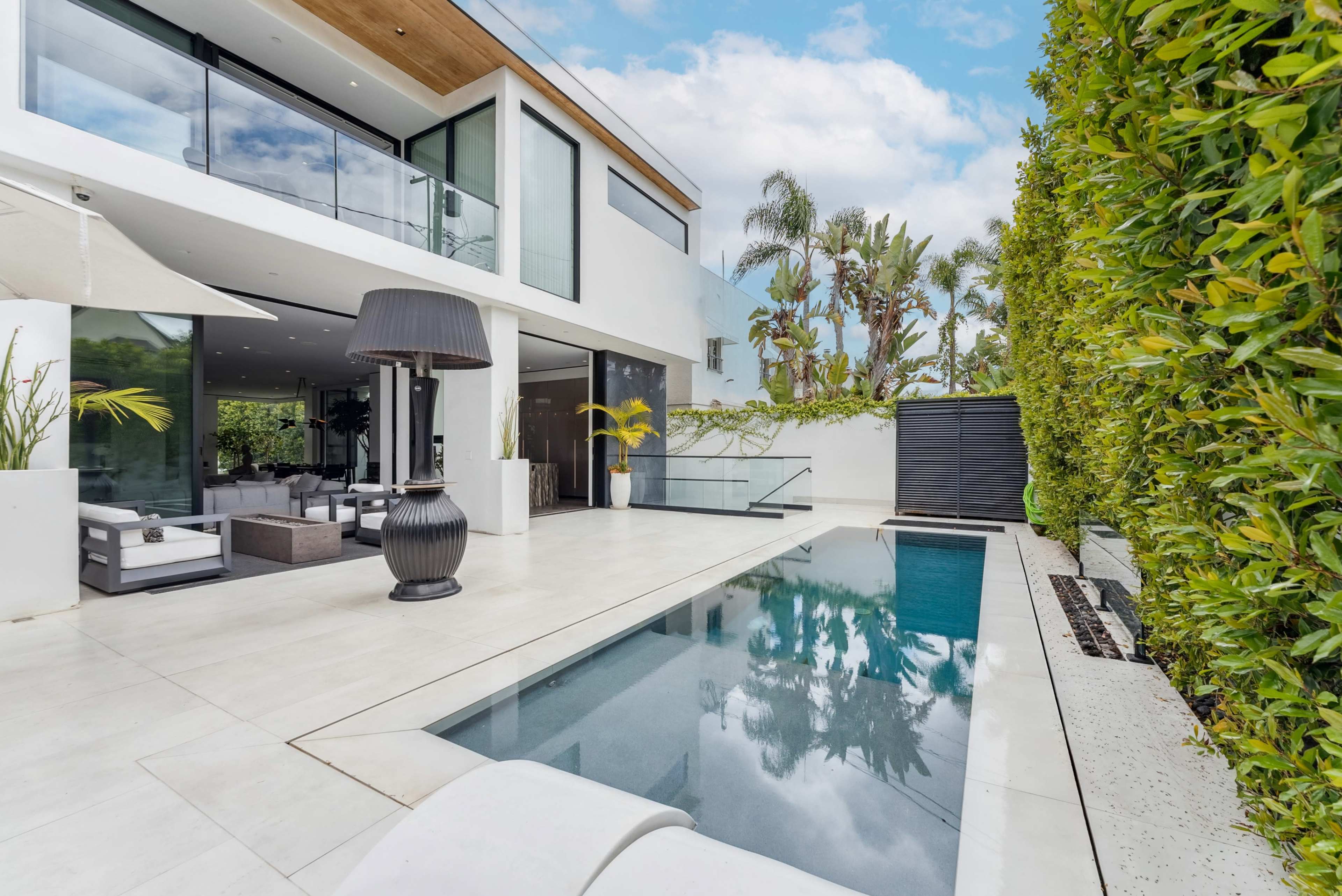 The image shows a modern two-story house with a swimming pool, surrounded by green landscaping and large windows.