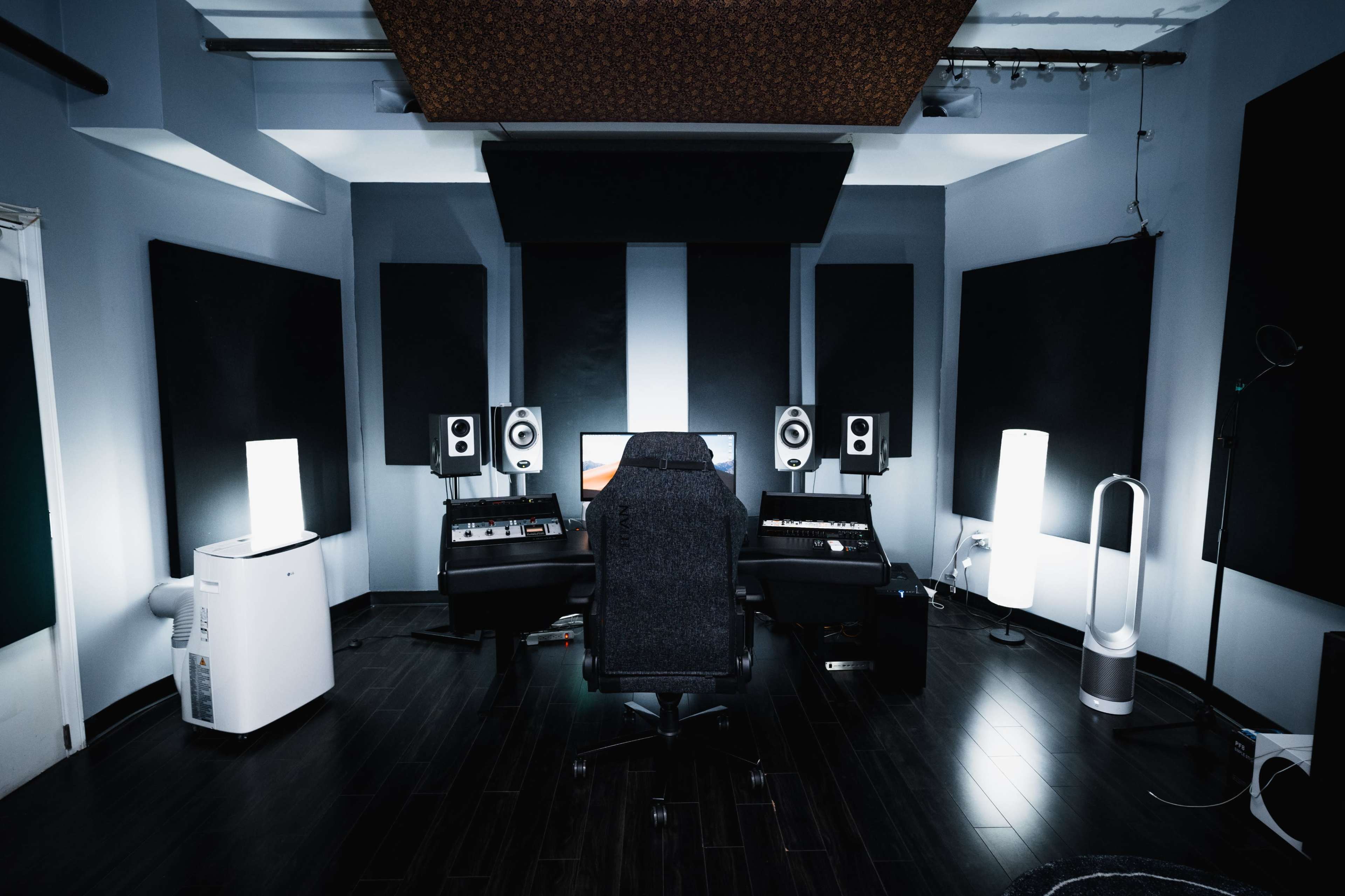 A well-equipped music studio with a central black chair, surrounded by soundproof panels, speakers, and various audio equipment.