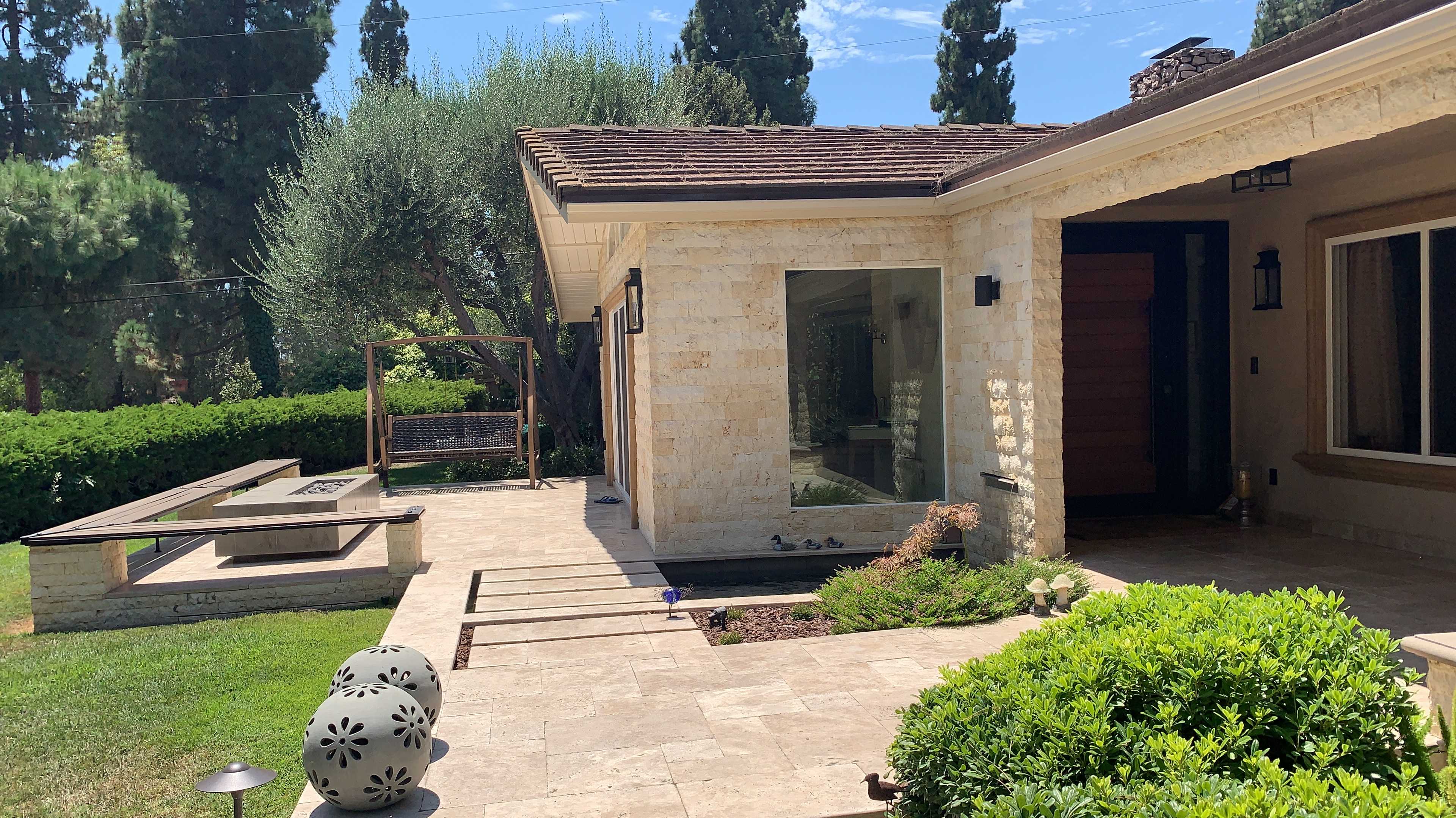 A modern stone house with a landscaped garden, featuring a stone pathway, a glass window, and a wooden swing set.