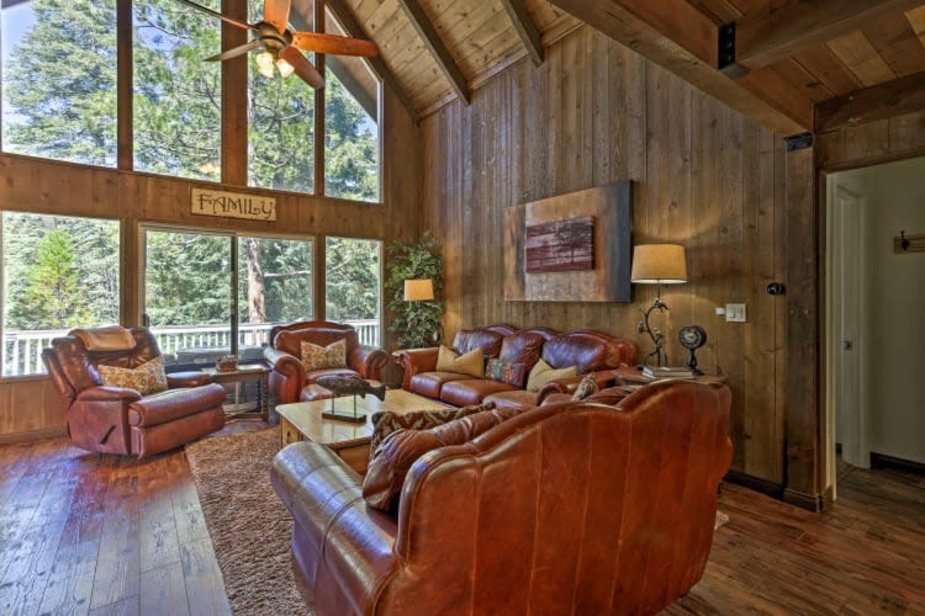 The living room features a high wooden ceiling, large windows, and rustic leather furniture arranged around a coffee table on a textured rug.